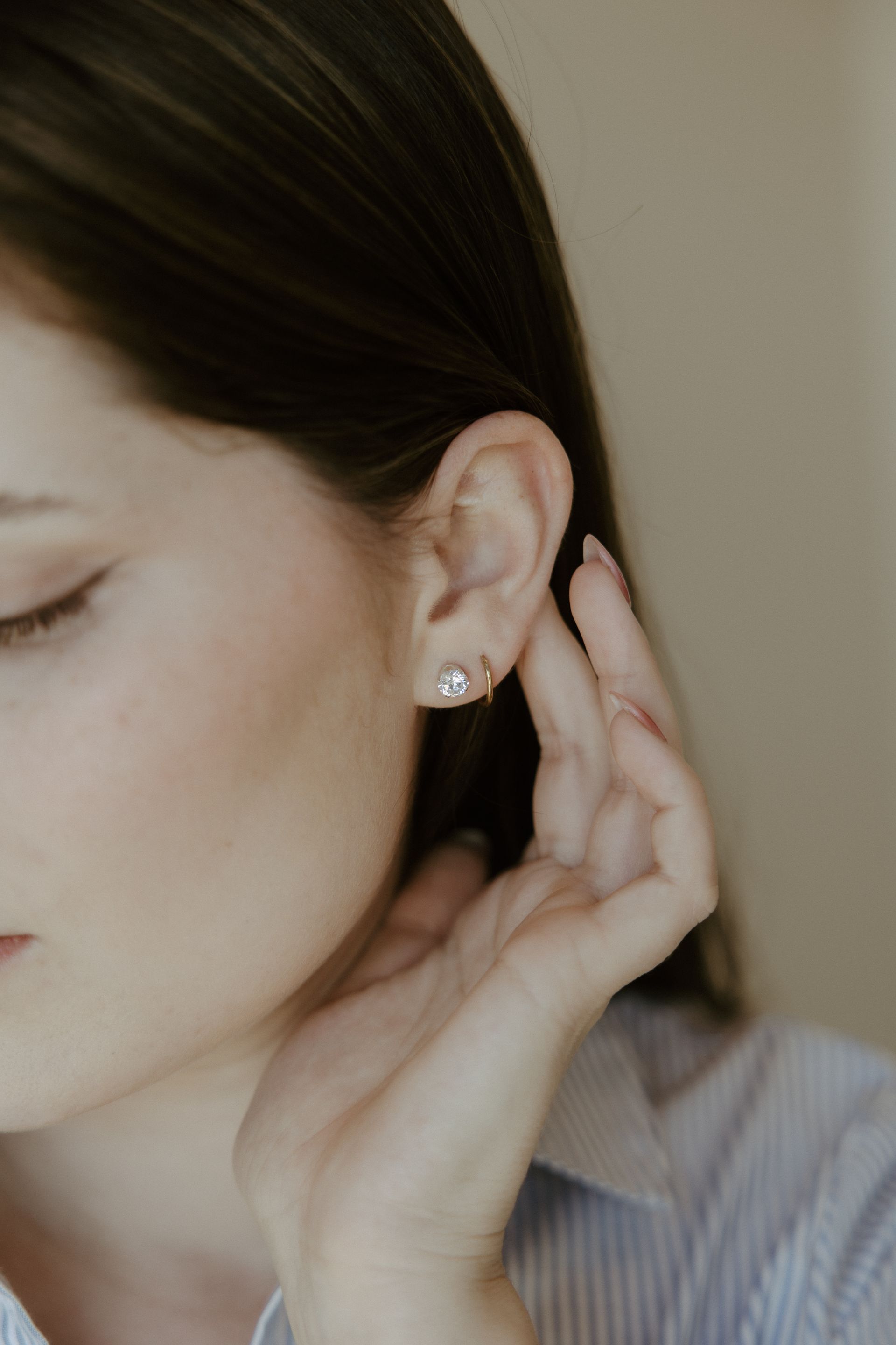 Woman touching her ear with a pearl earring, closed eyes, soft lighting.