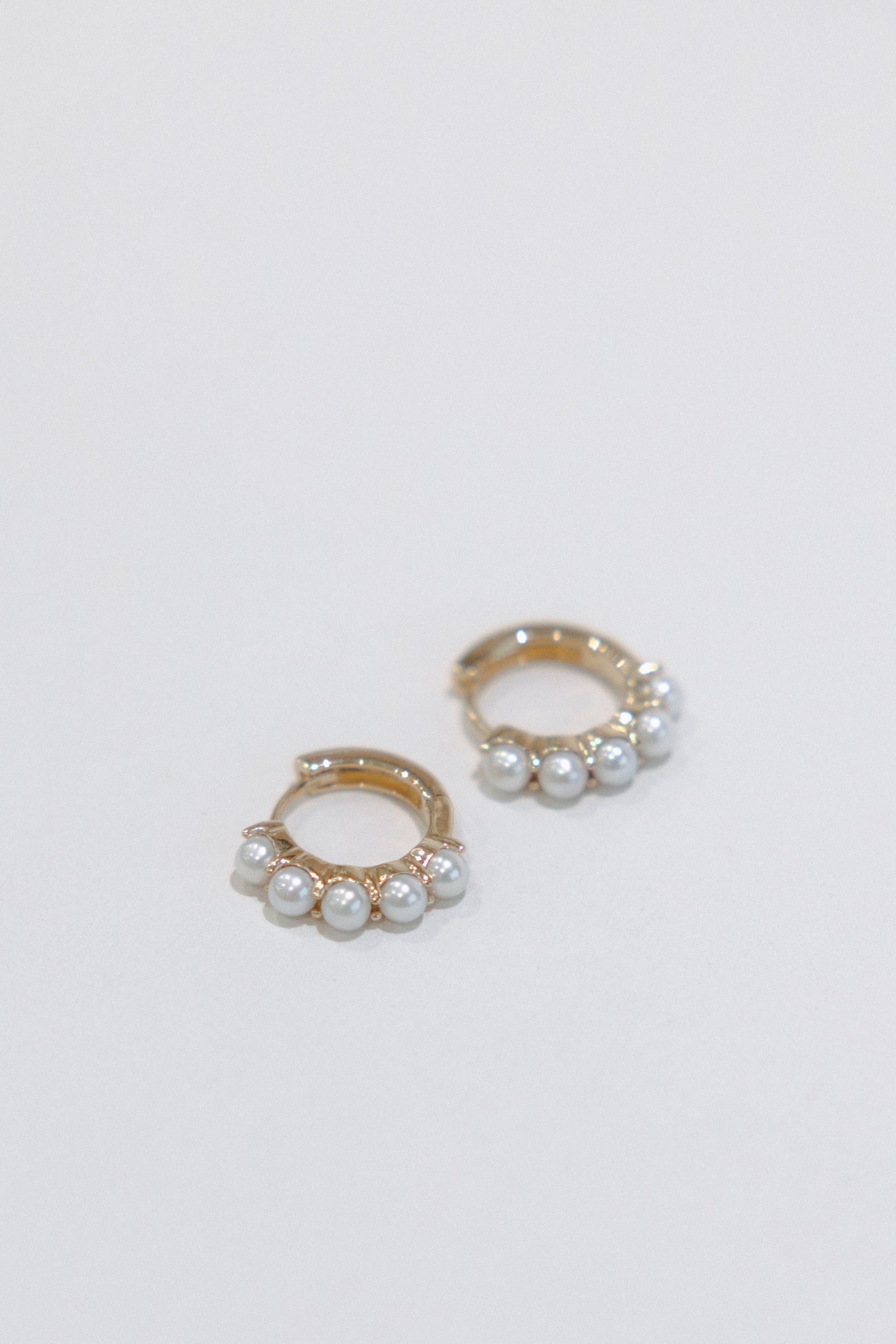 Gold hoop earrings with a row of small, white pearls on a white background.