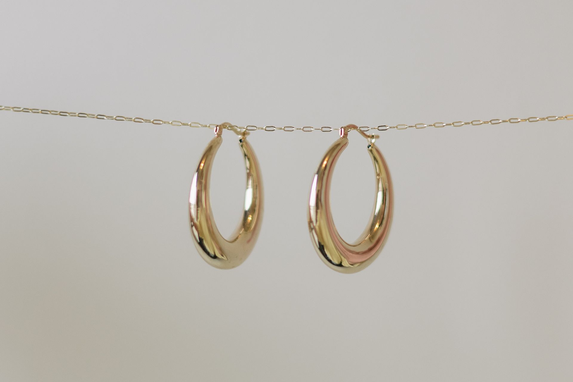 Pair of gold hoop earrings hanging on a delicate gold chain against a white background.