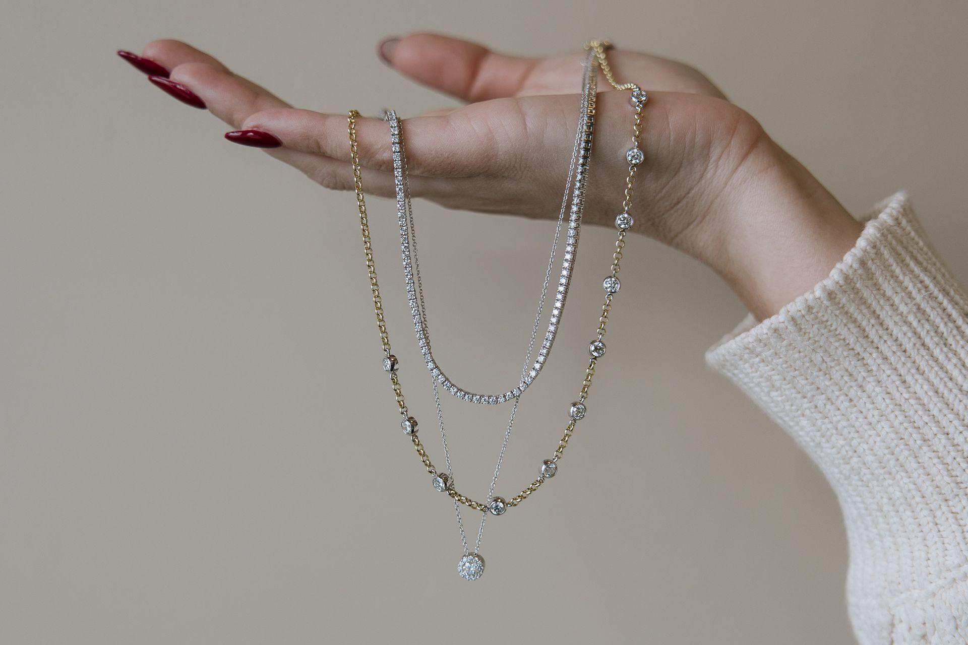 Hand holding three diamond necklaces against a neutral background.