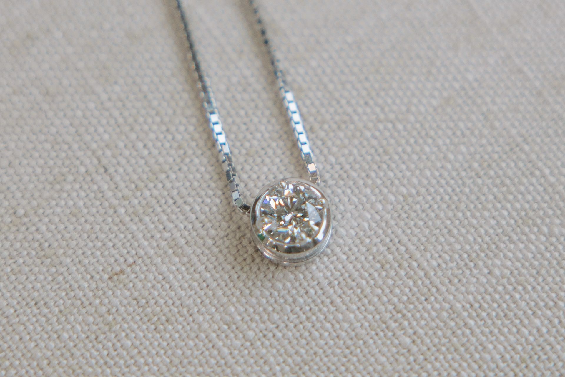 Diamond pendant necklace on a silver chain, resting on a beige surface.