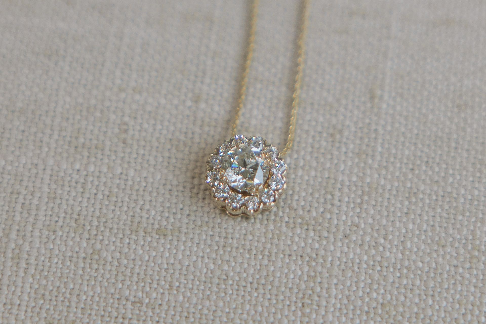 Gold necklace with a diamond pendant on a beige surface.