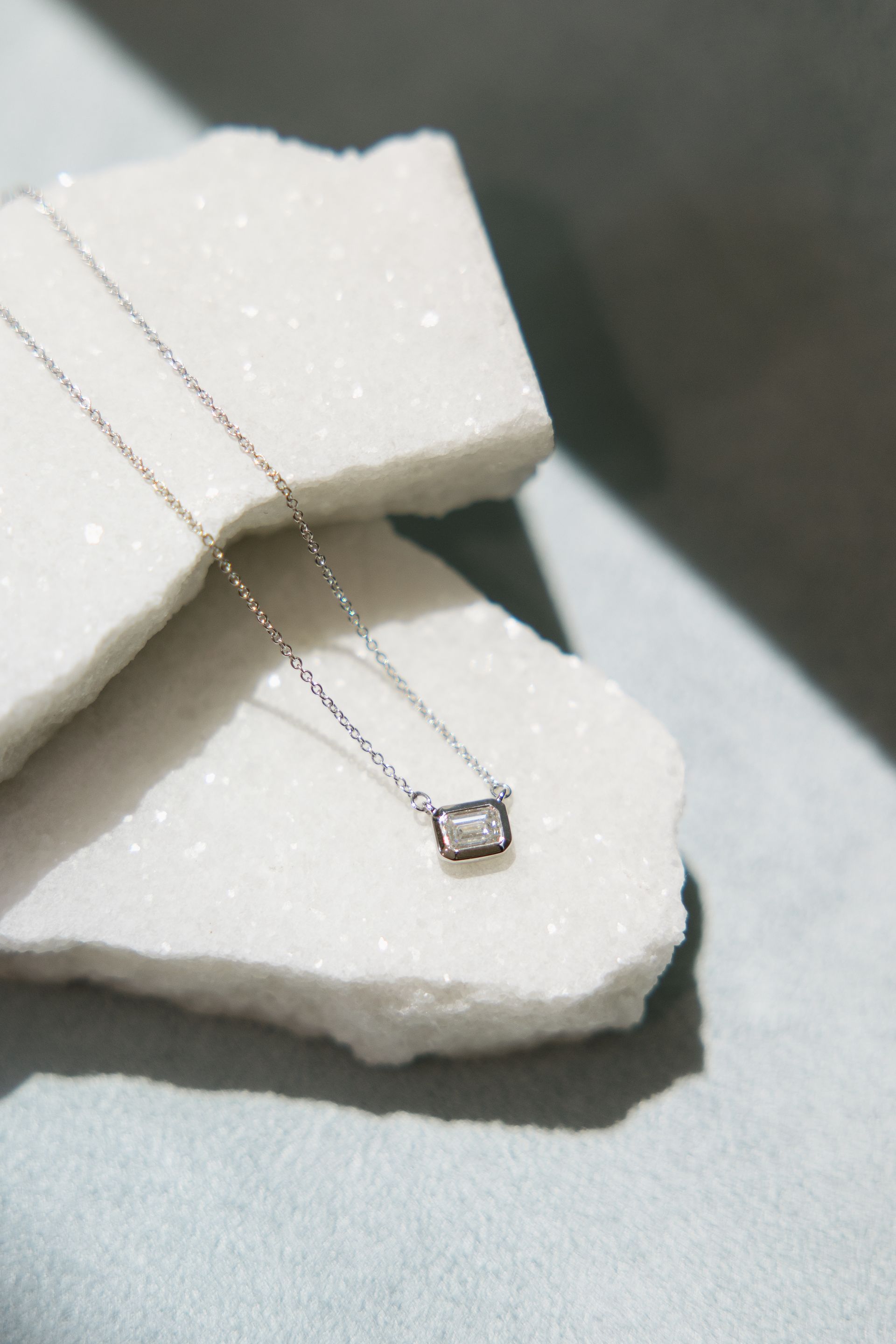 Silver necklace with a rectangular pendant on a white marble surface.