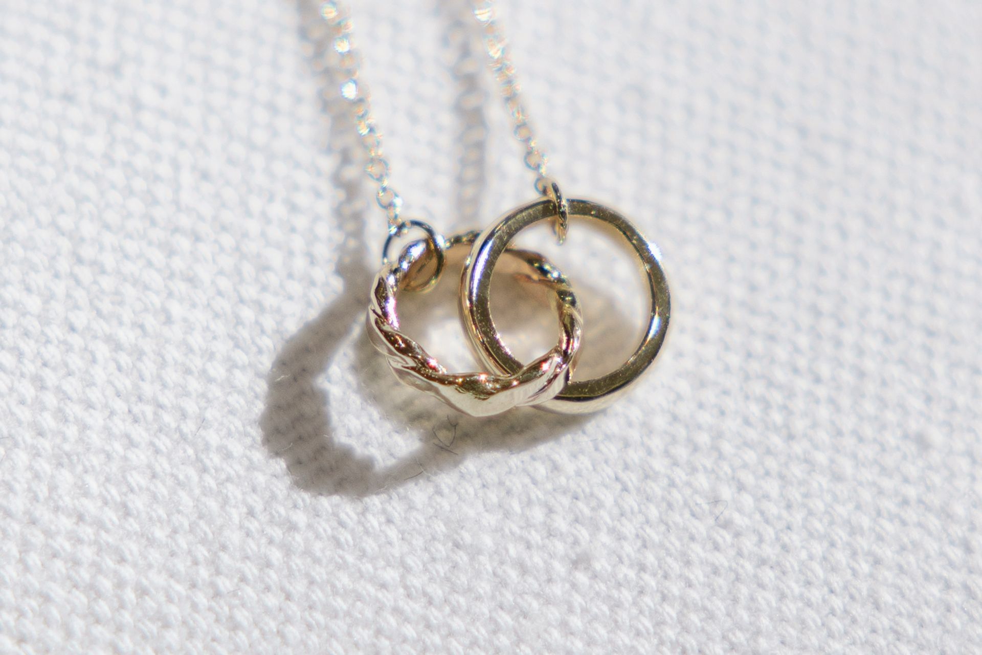 Silver necklace with two intertwined circles on white fabric.