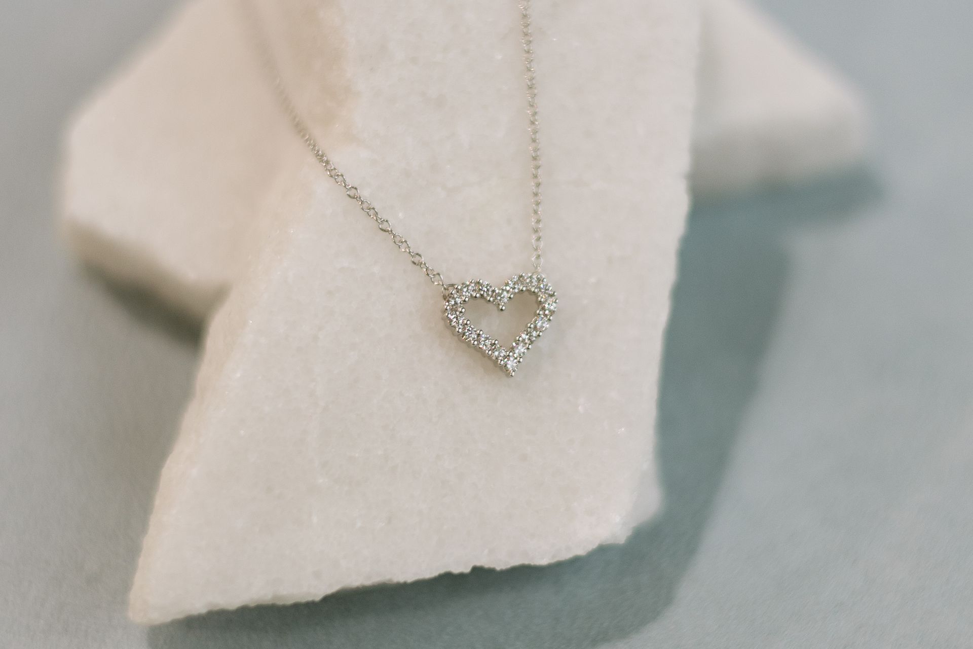 Silver heart-shaped necklace with small stones, resting on a white, textured surface.