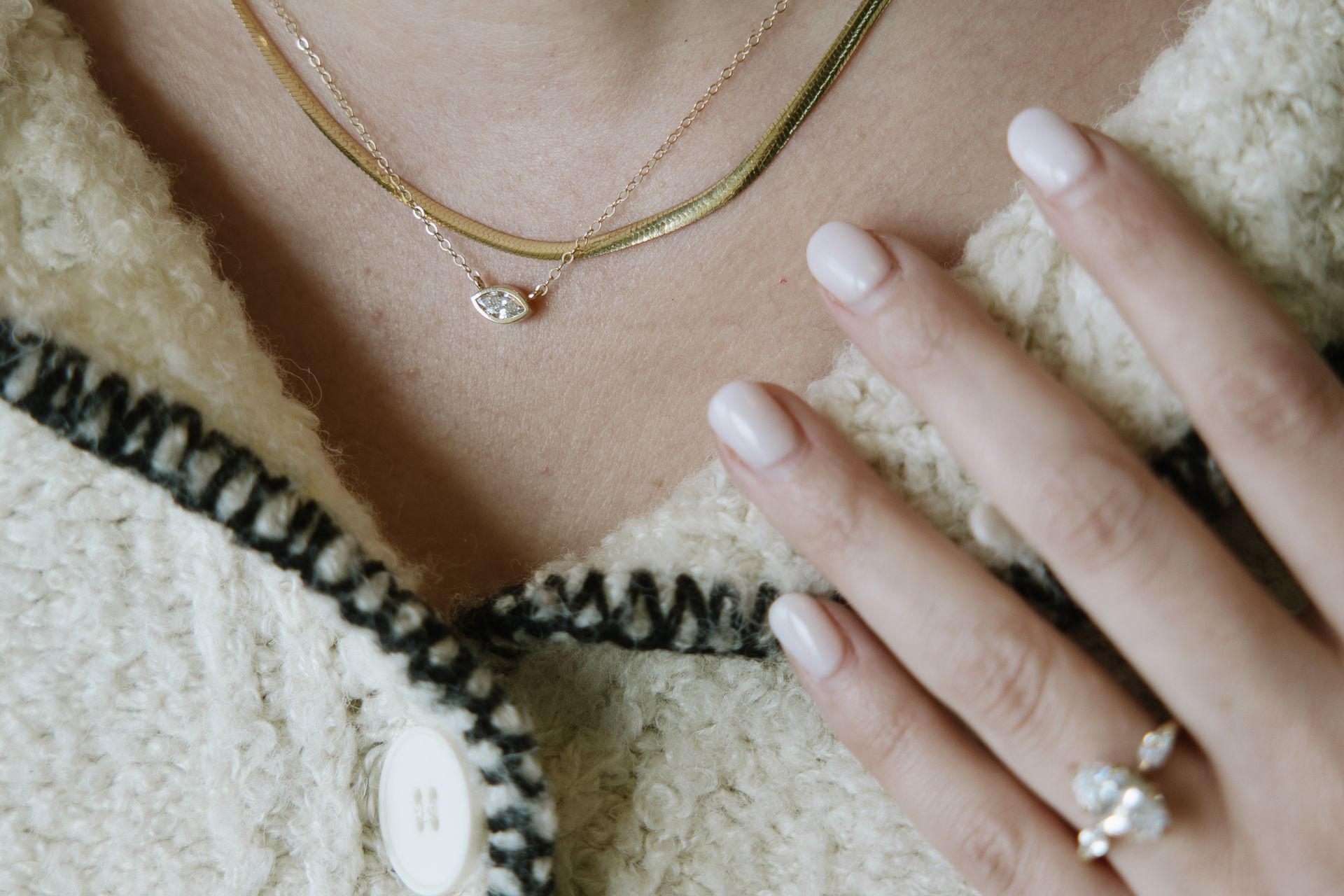 Woman wearing gold necklaces and ring, hand resting on sweater.