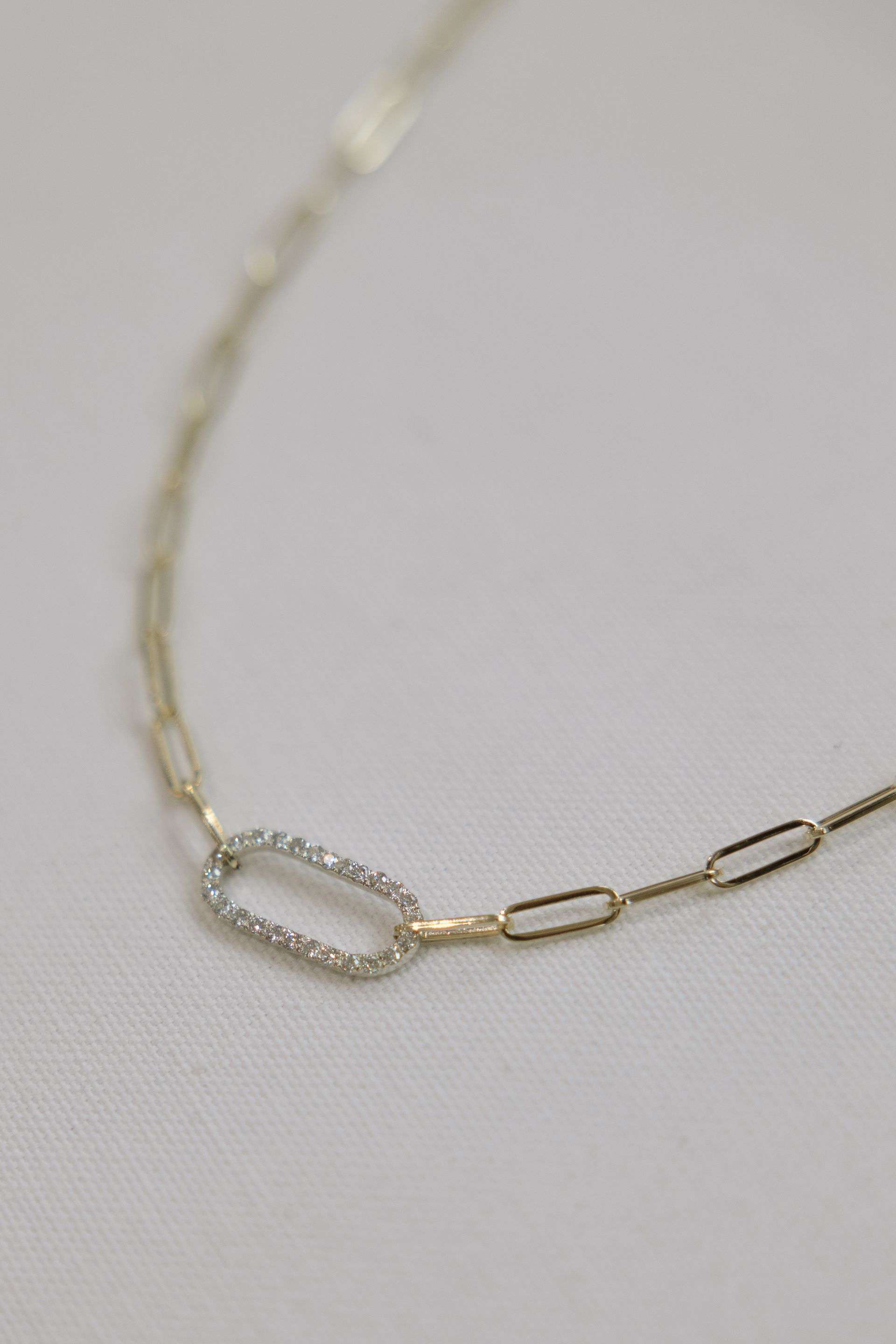 Gold chain necklace with a central diamond-studded oval link and paperclip chain links.
