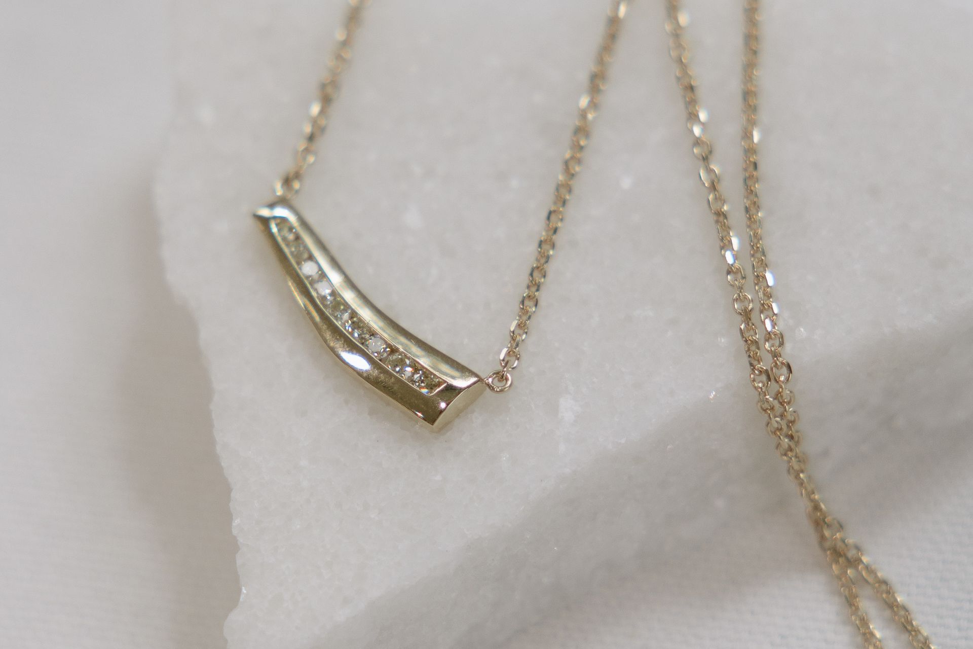 Gold necklace with diamonds on a white surface.