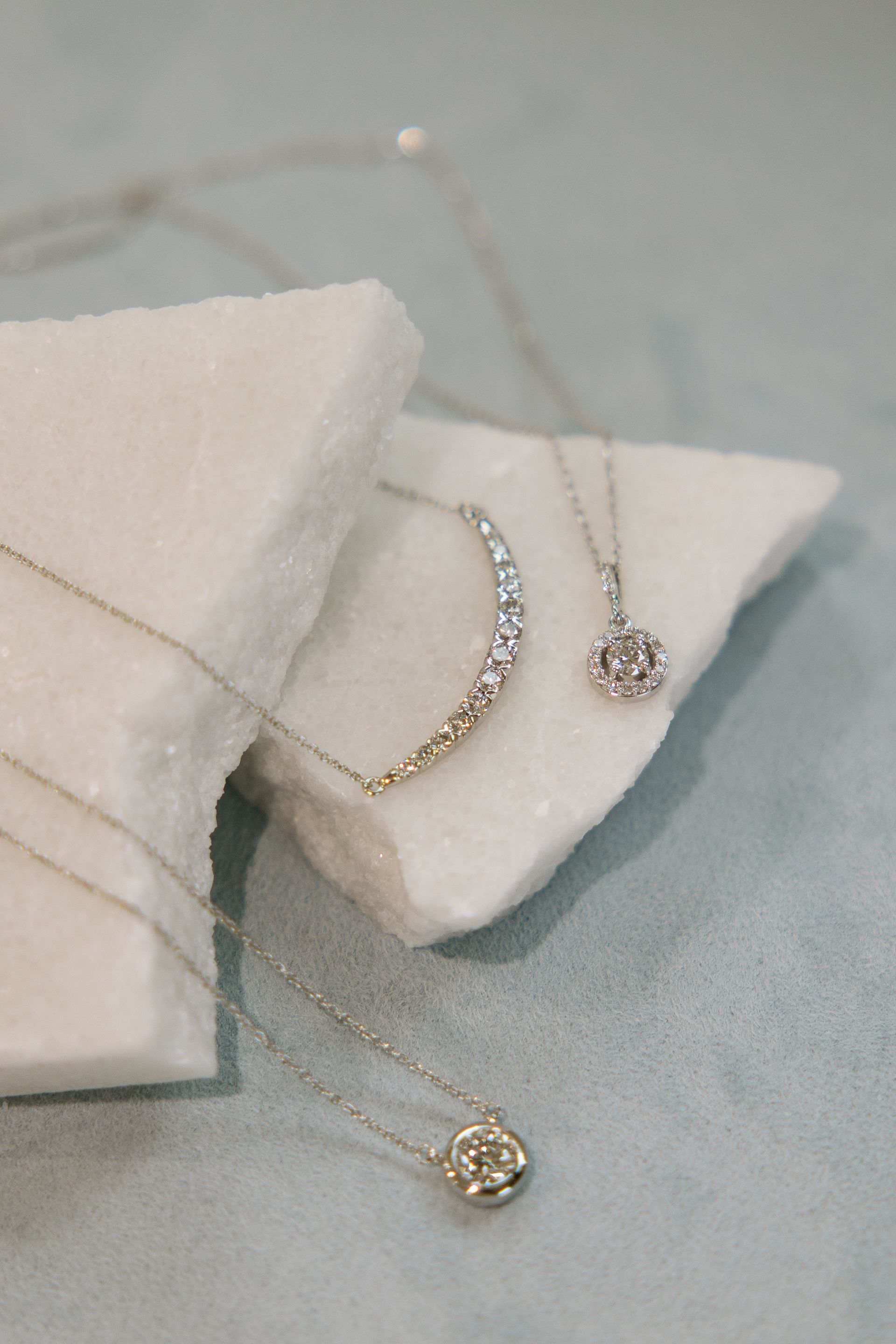 Jewelry necklaces displayed on a white textured surface with a light blue backdrop.