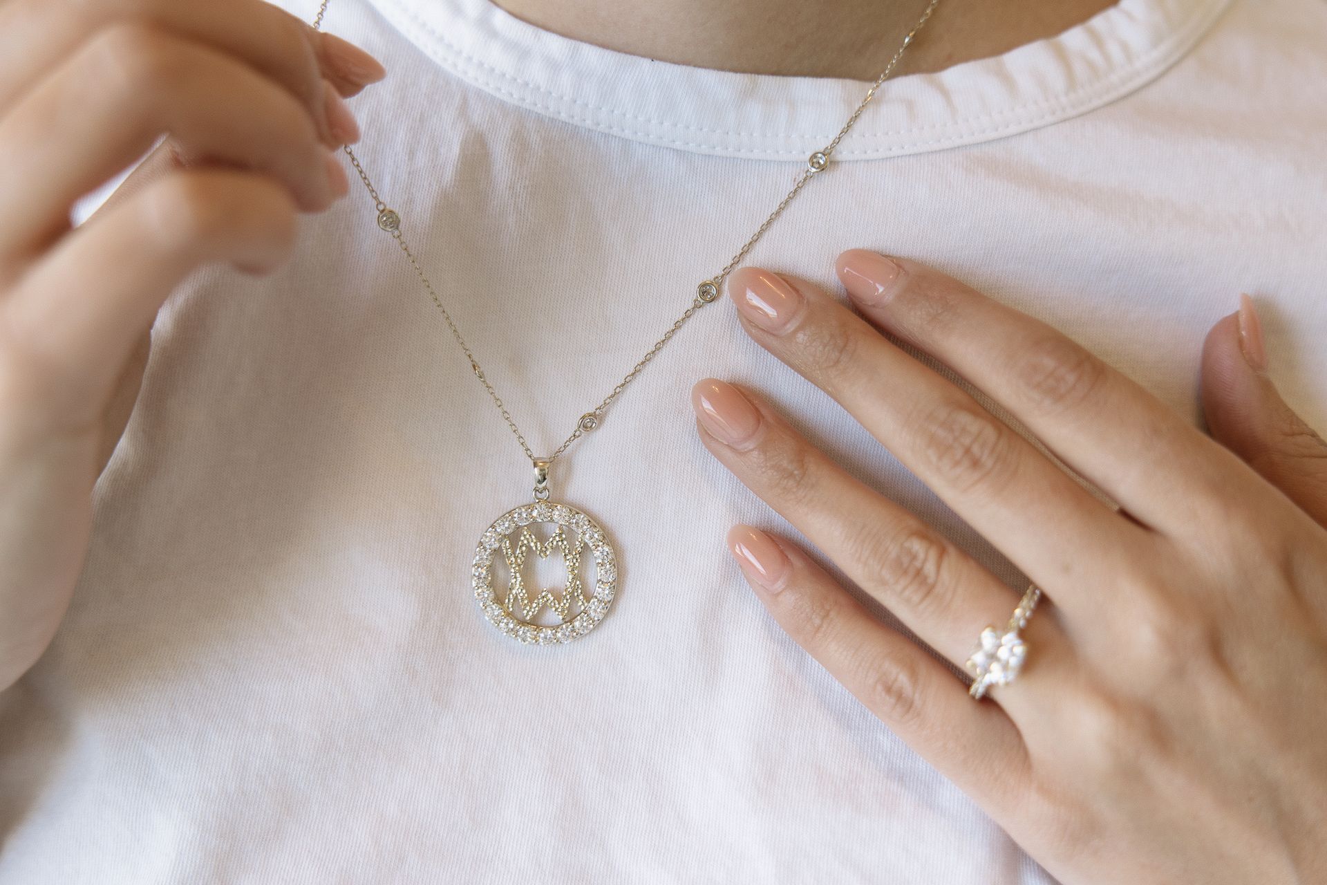 Person wearing a gold necklace with a pendant and a ring. White shirt.