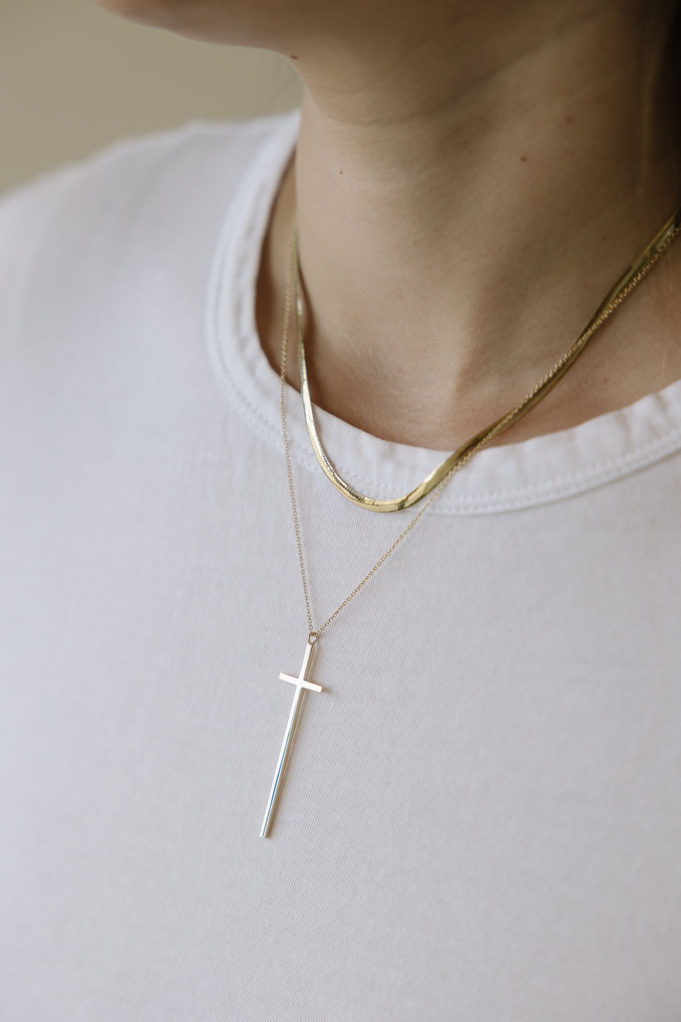 Person wearing two gold necklaces: one a layered chain, the other a cross pendant with rhinestones.