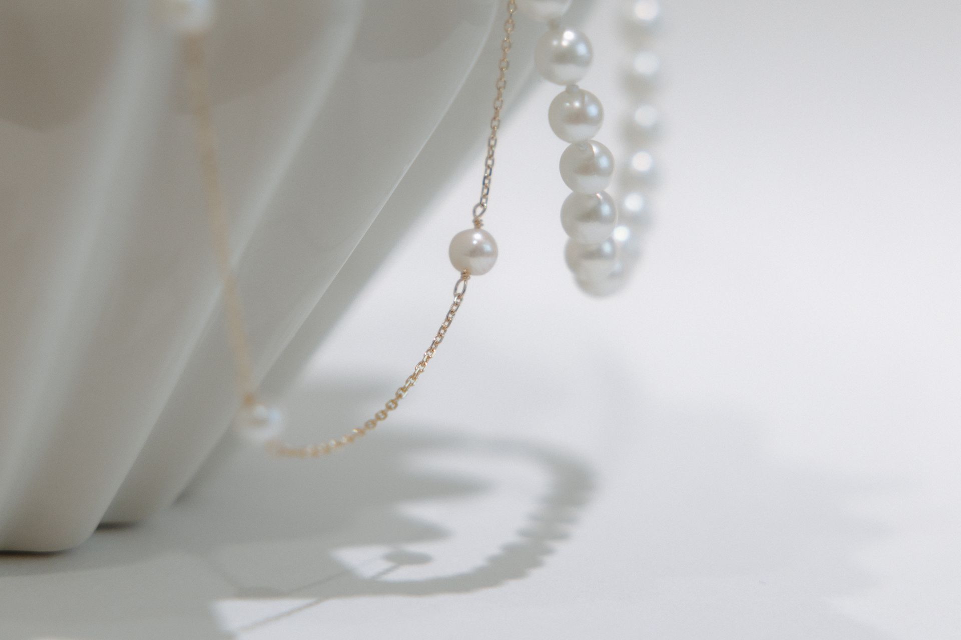 Pearl necklace draped over white ribbed vase.