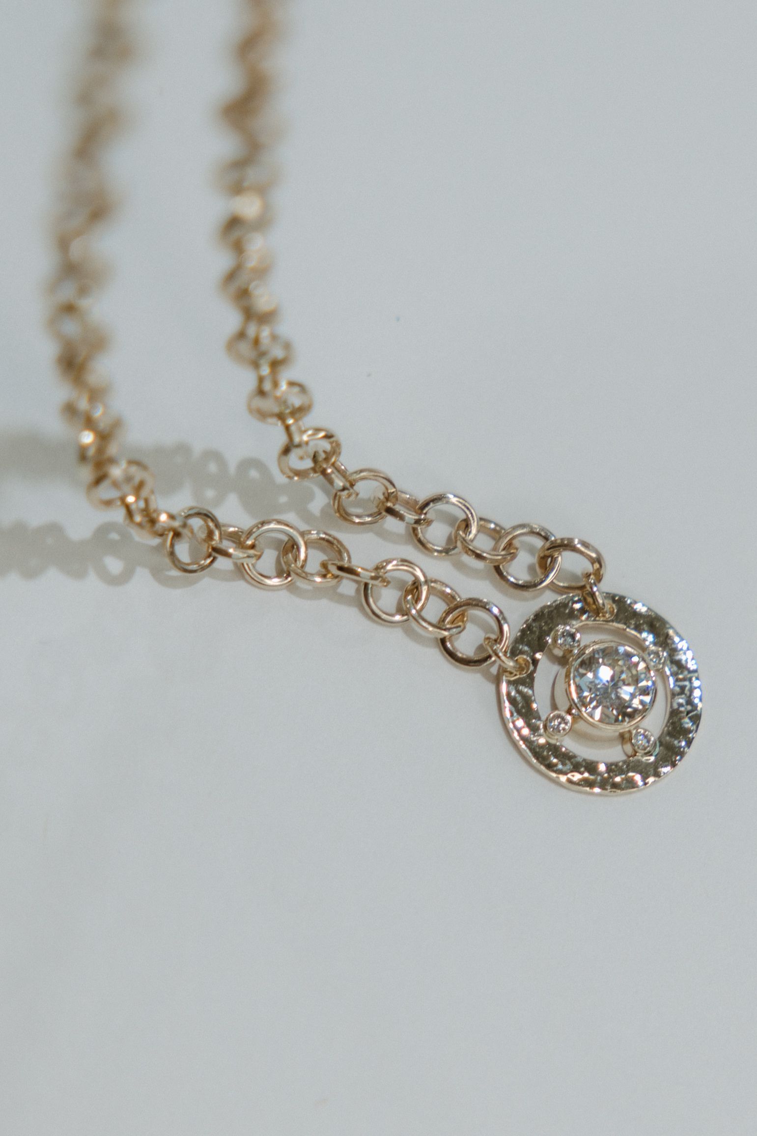 Gold necklace with a diamond pendant on a white surface.