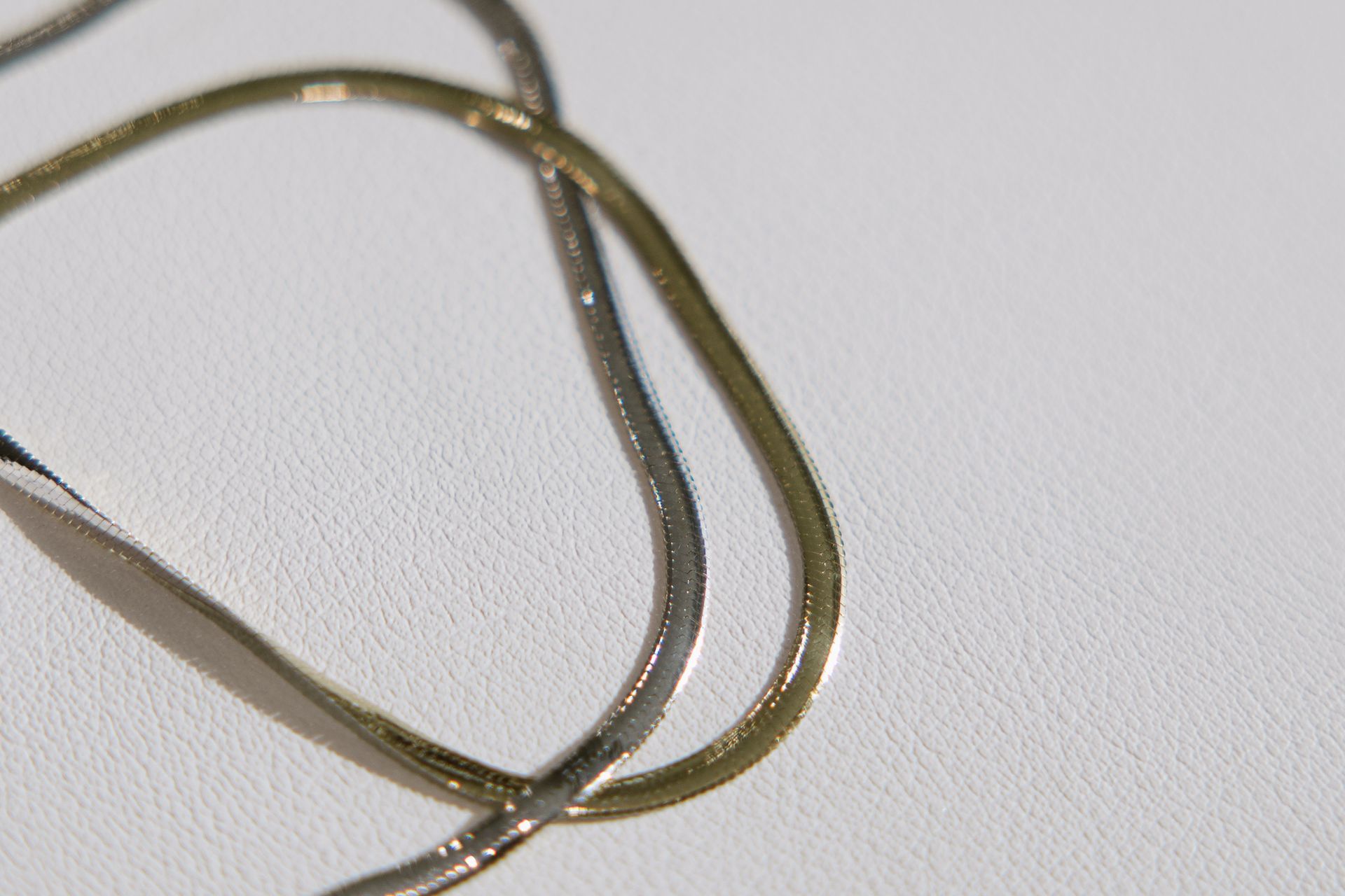 Two intertwined gold and silver necklaces on a white surface.