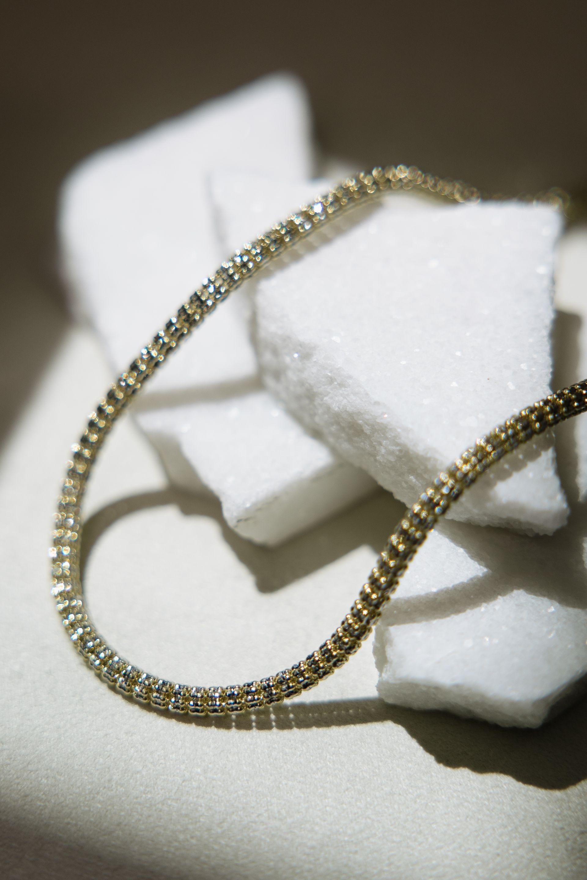Gold chain necklace draped across white, textured blocks.