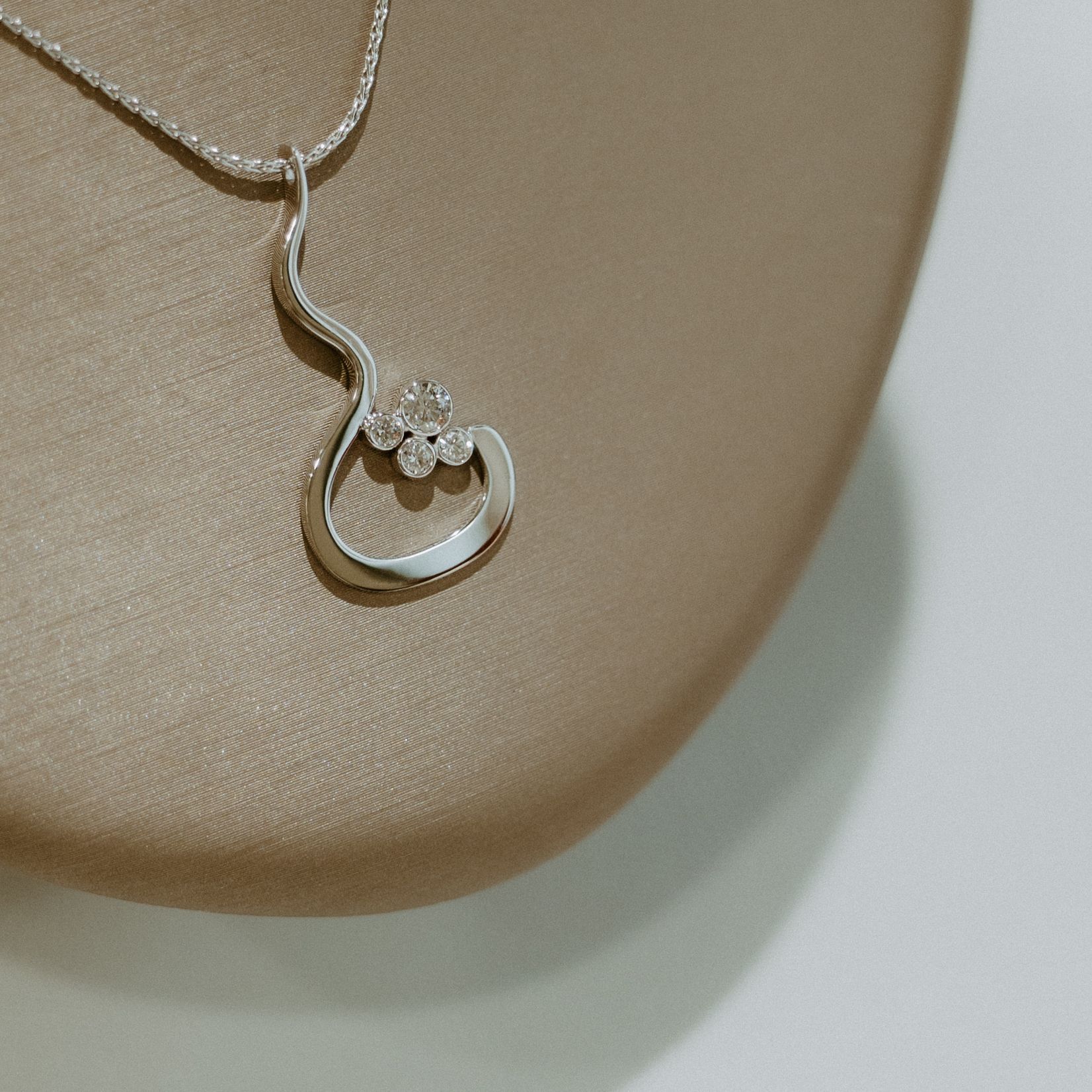 Silver necklace with a curved pendant, set with small sparkling gemstones, on a display.