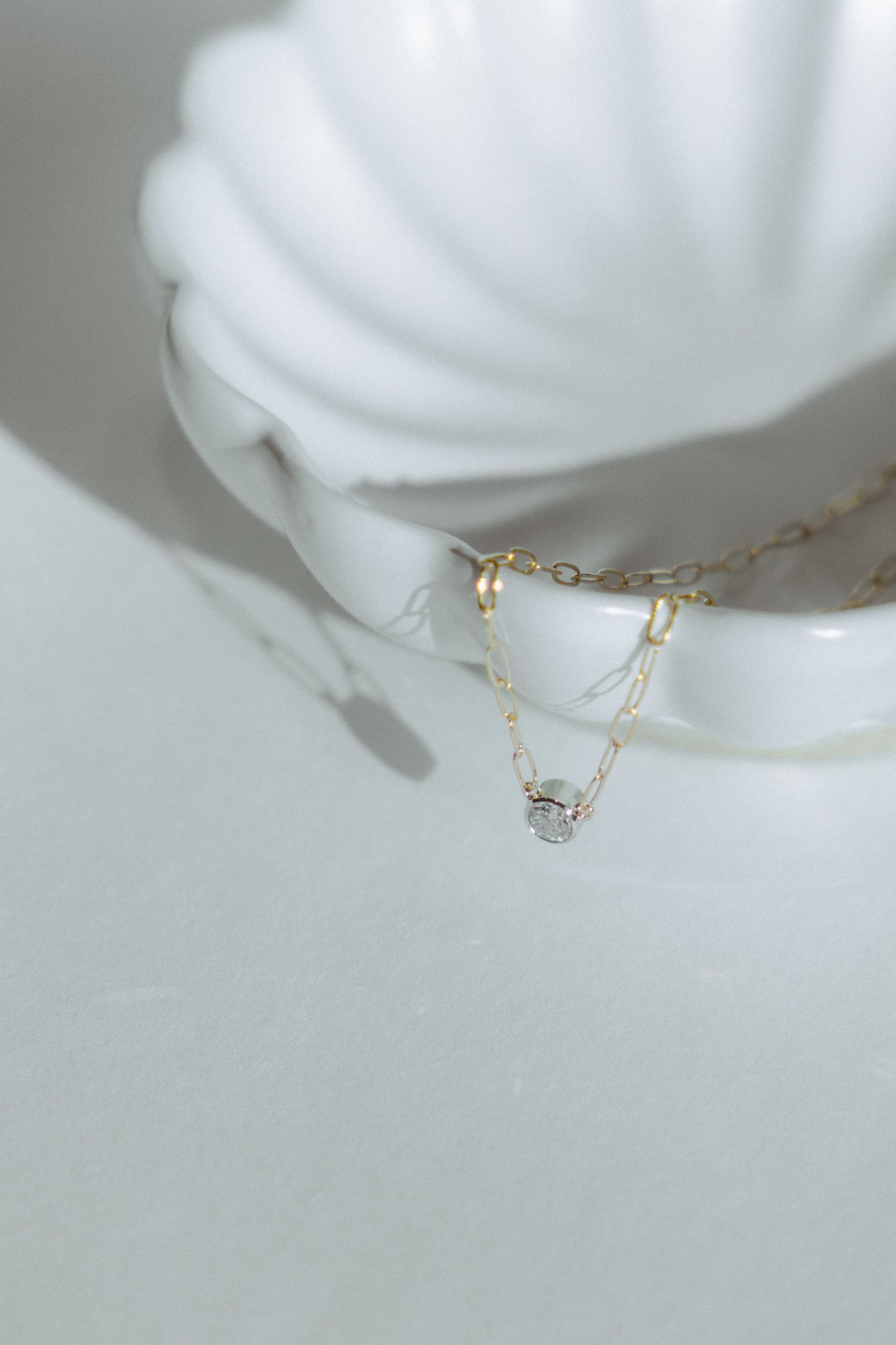 Gold necklace with a small pendant rests in a white, decorative shell.