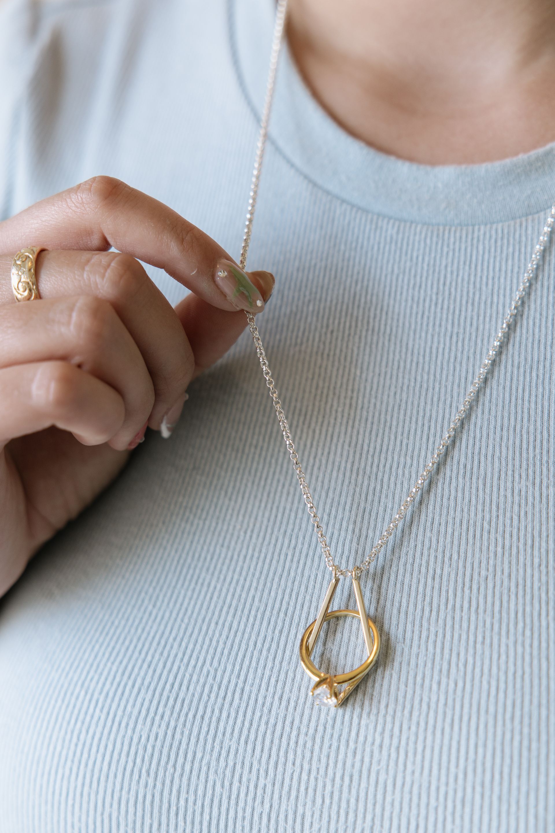 Woman holding a silver necklace with a gold pendant, wearing a light blue shirt.