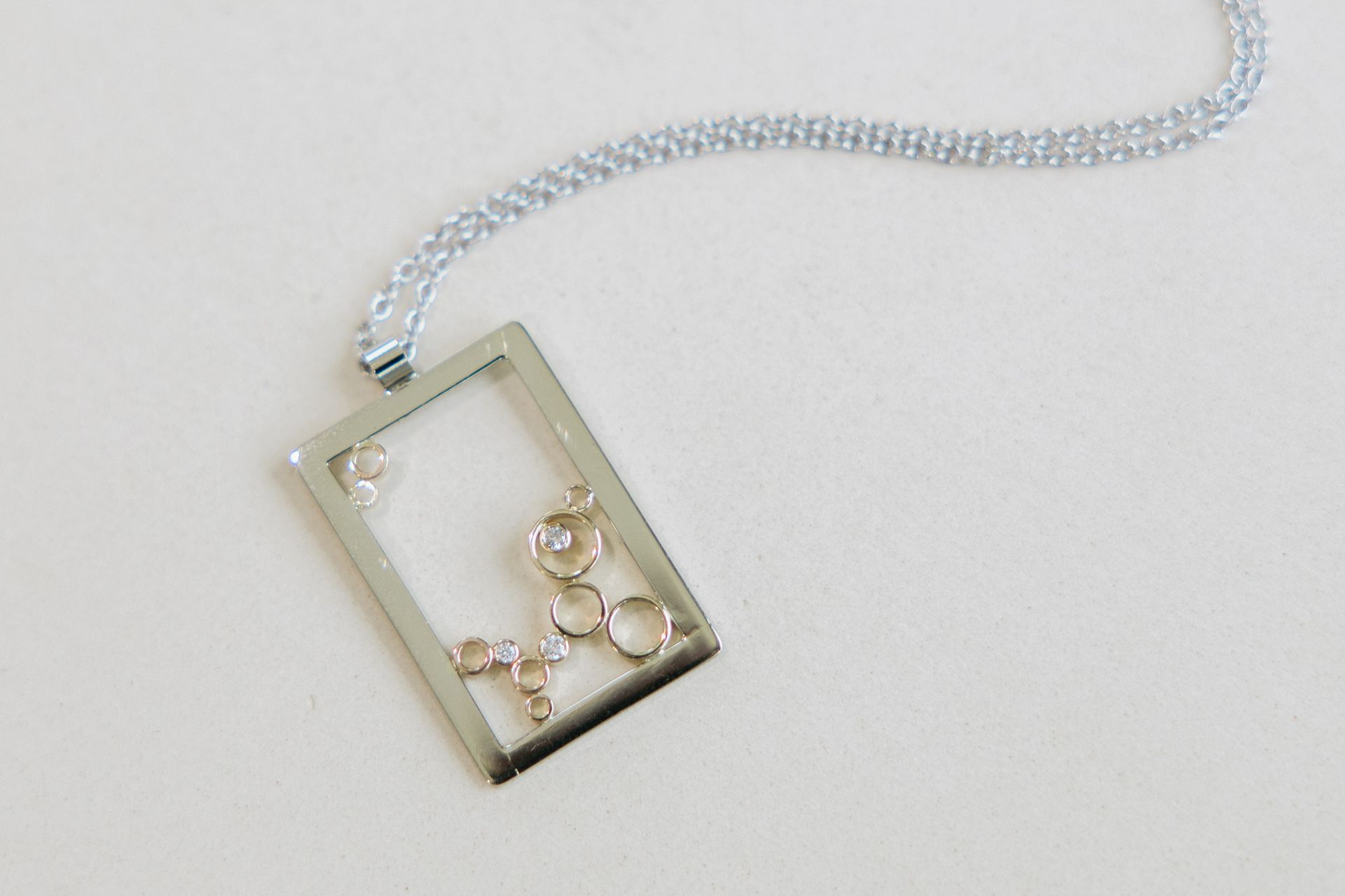 Silver rectangular pendant necklace with delicate, interior charms on a white surface.
