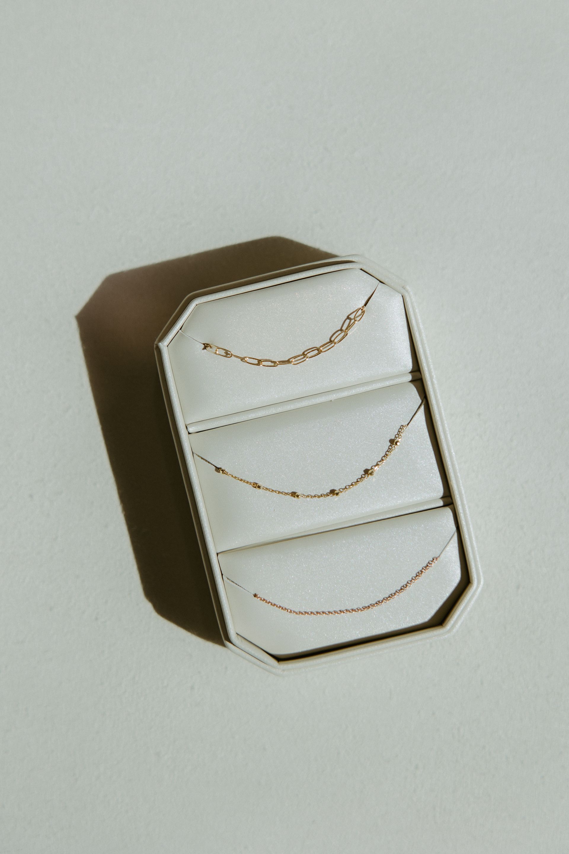 Jewelry box with three gold necklaces on a white surface. Brown box with octagonal shape.