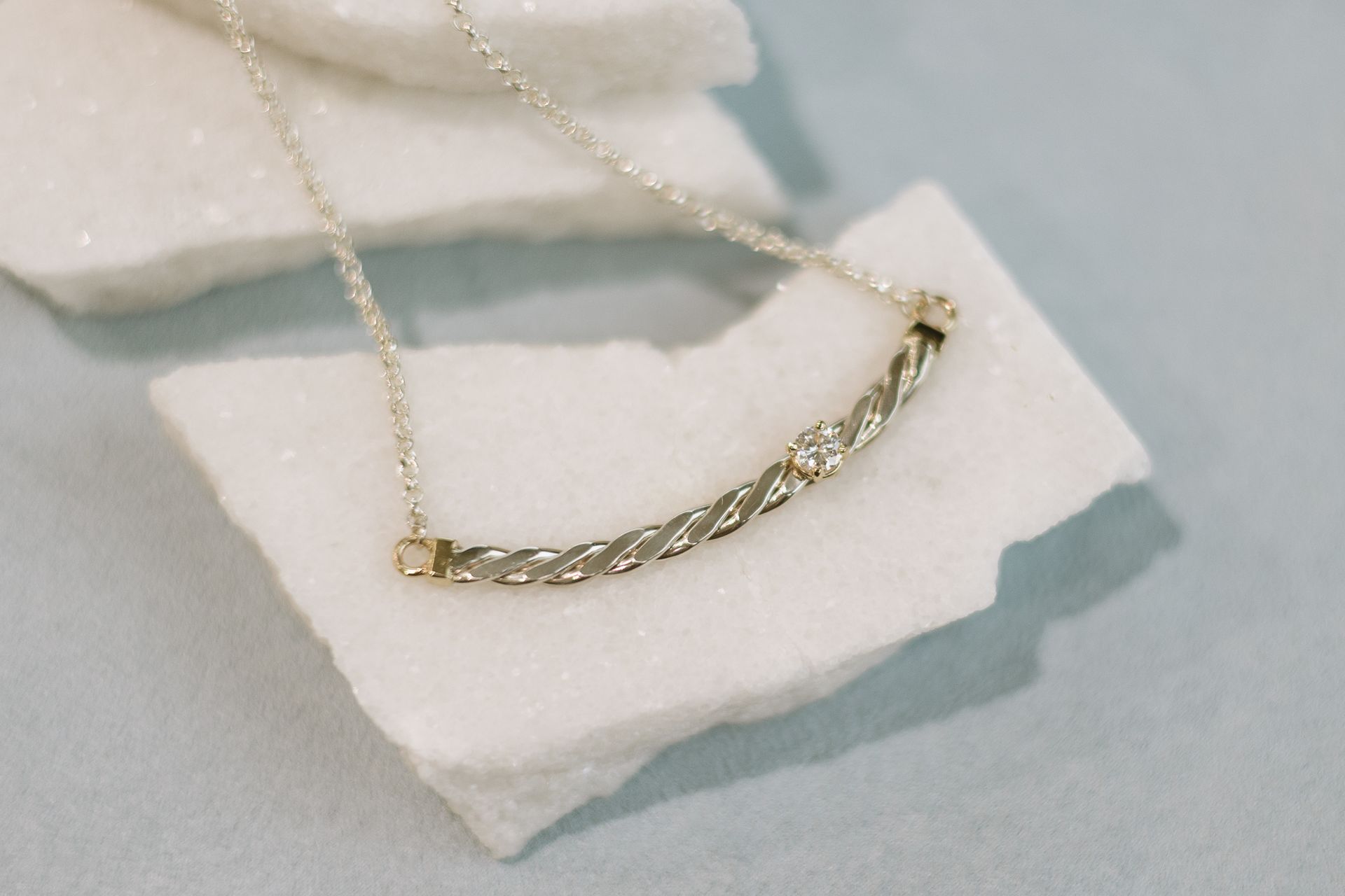 Gold necklace with a curved, twisted bar pendant, resting on white, textured surface.
