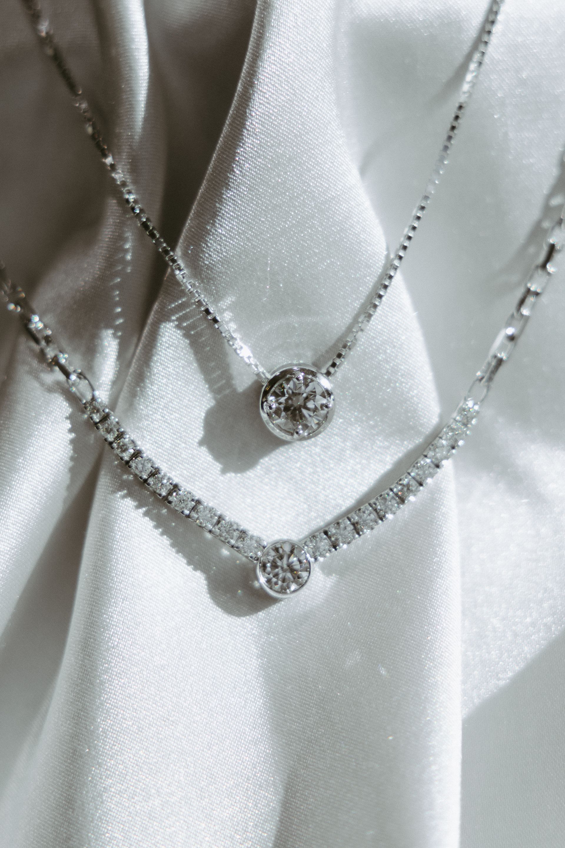Two diamond necklaces on white satin fabric.