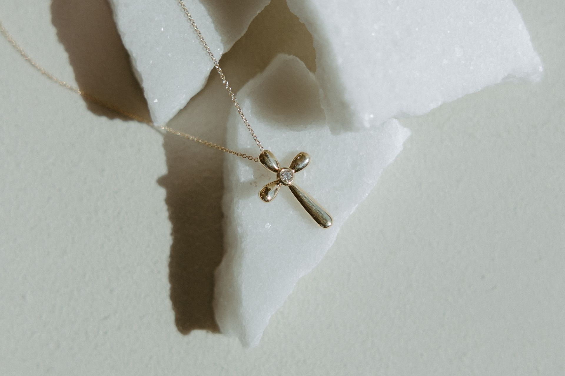 Gold cross pendant necklace on white, textured surface.