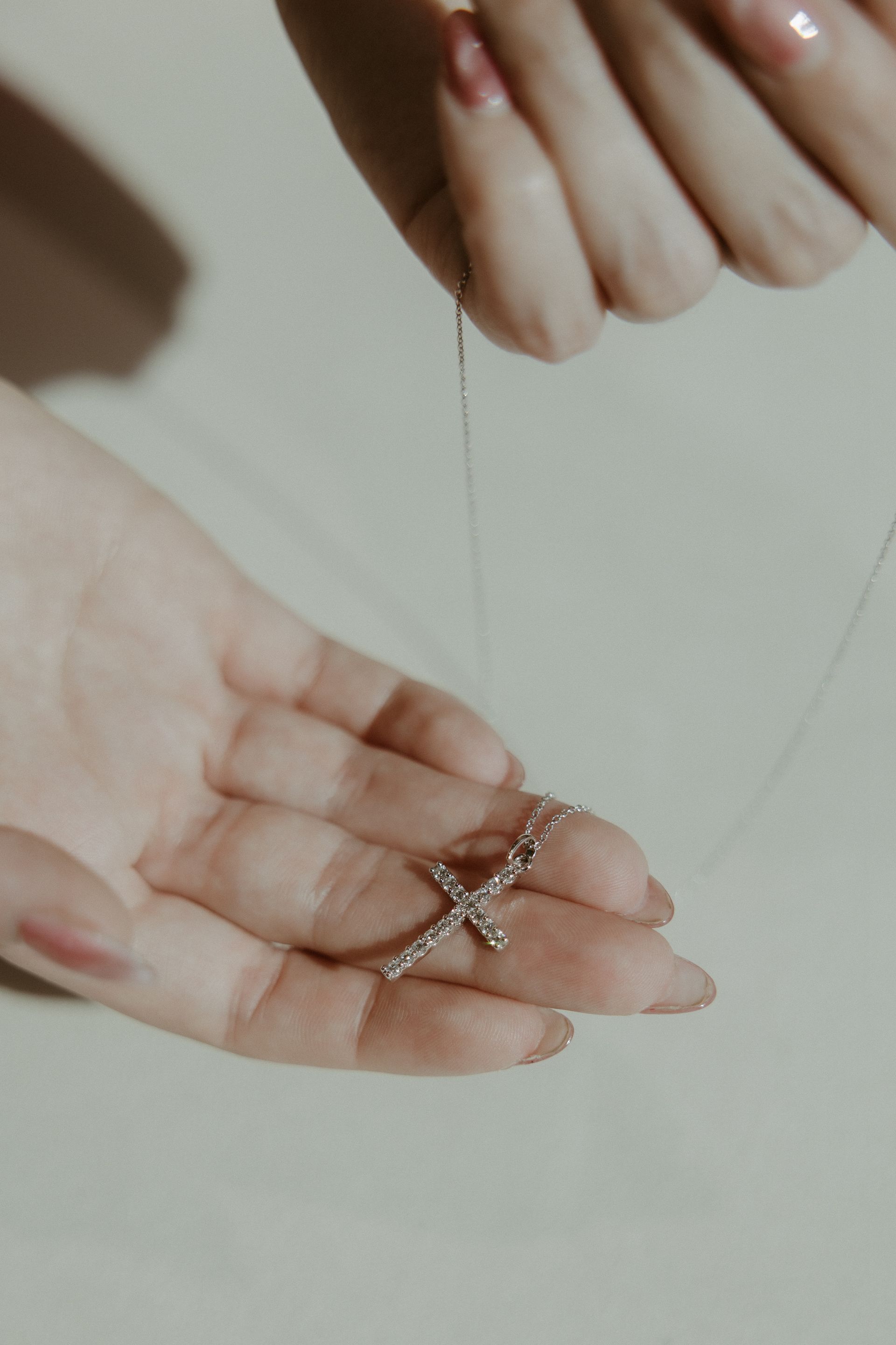 Hands holding a silver cross necklace.