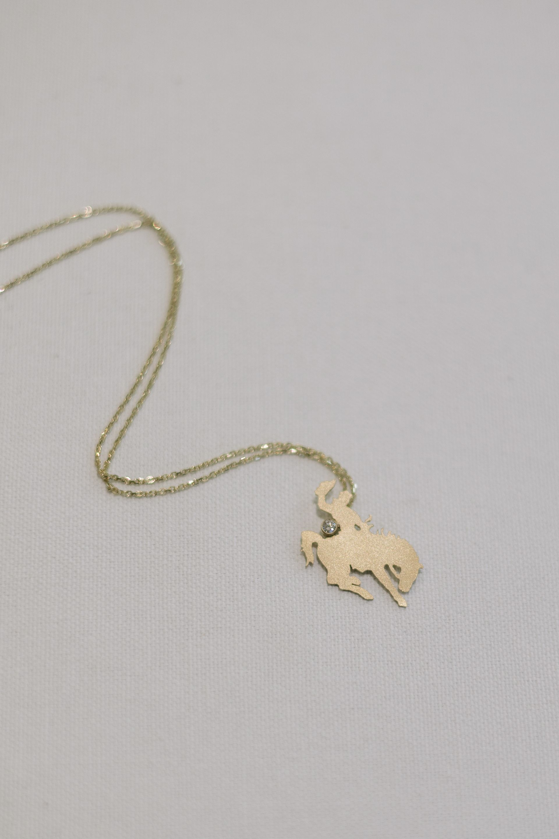 Gold necklace with a cowboy silhouette pendant on a white background.