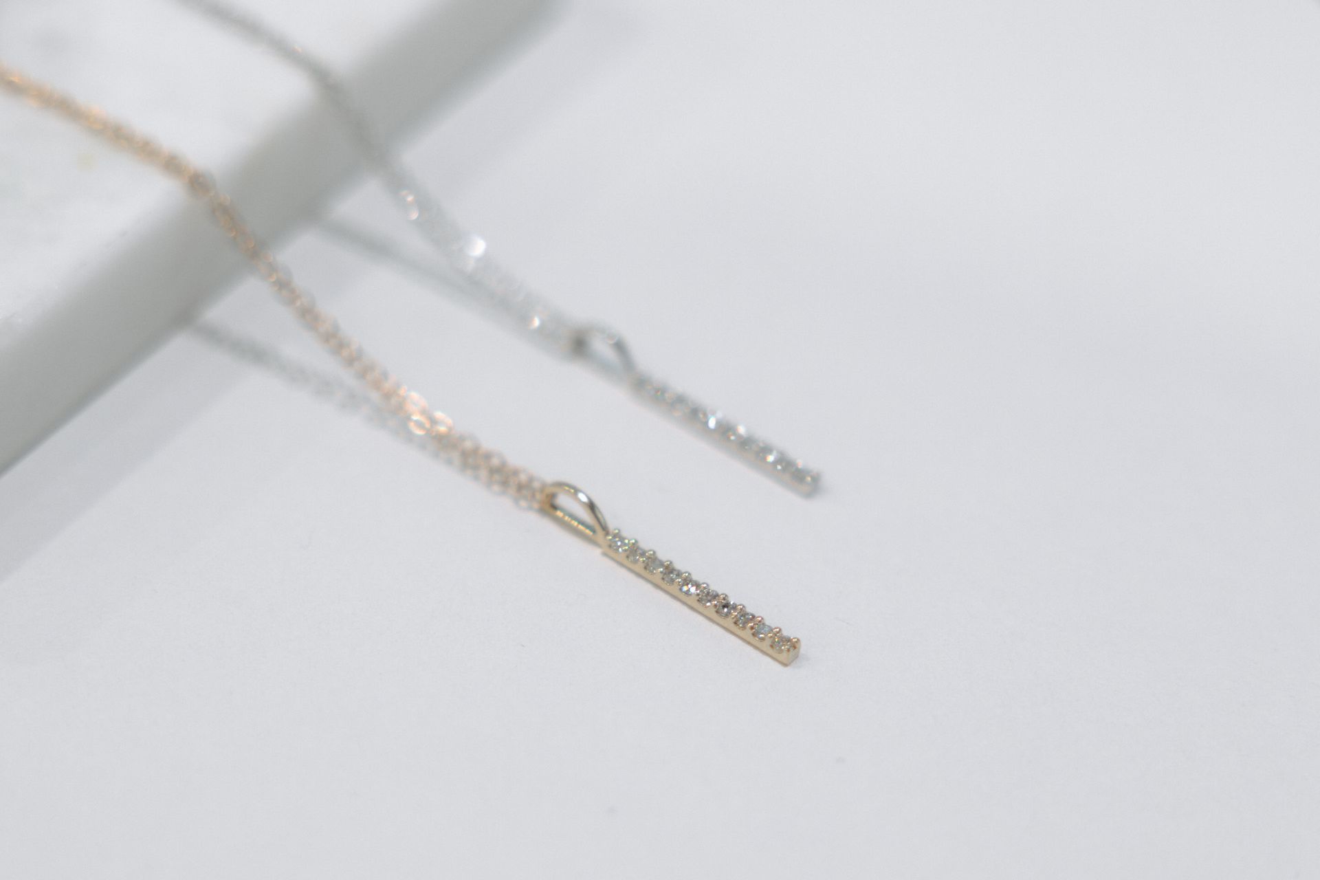 Two delicate necklaces, one gold and one silver, with a vertical bar pendant on a white surface.