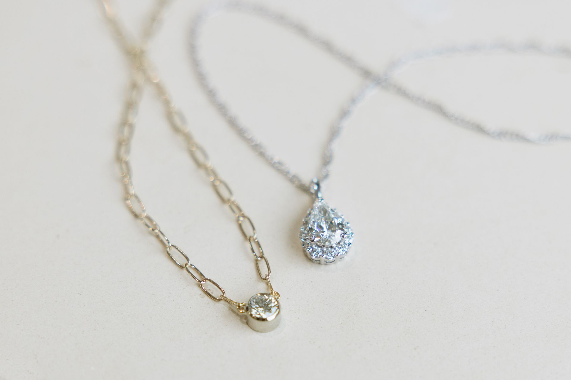 Two delicate necklaces: one gold chain with a single gem, the other silver with a teardrop pendant.