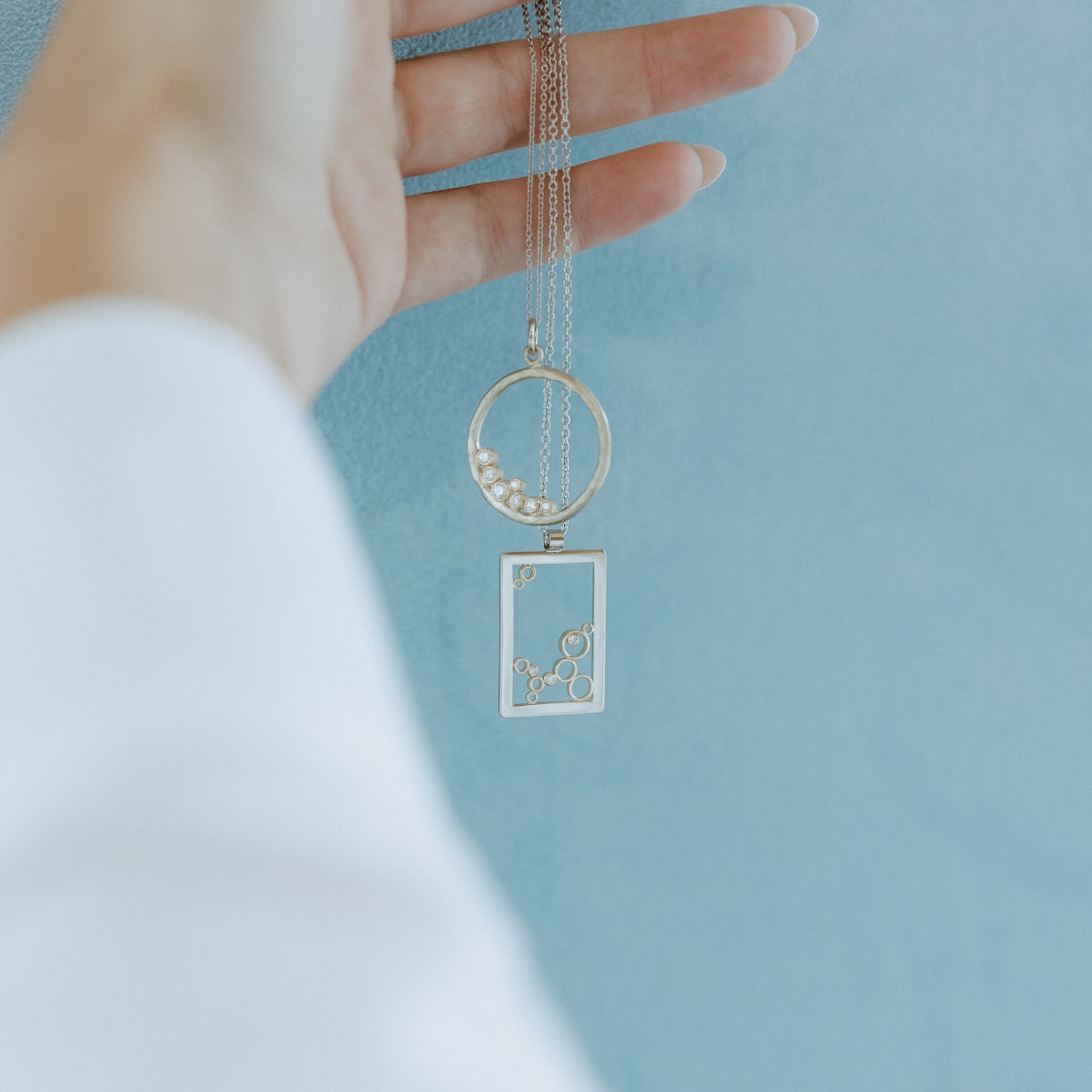 Hand holding a gold necklace with a circle and rectangle pendant filled with small, decorative elements.