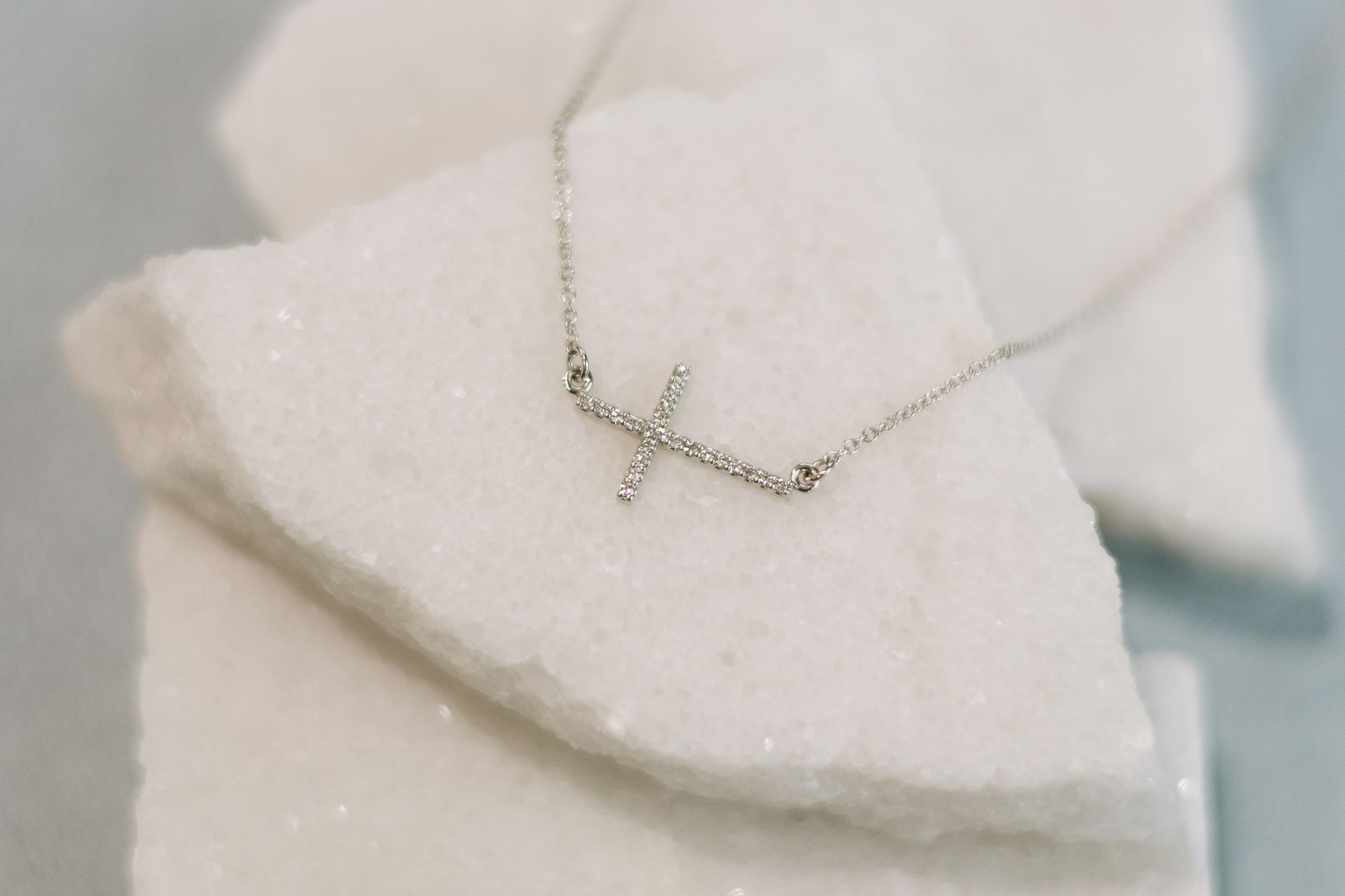 Silver necklace with a cross pendant resting on white, textured stone pieces.