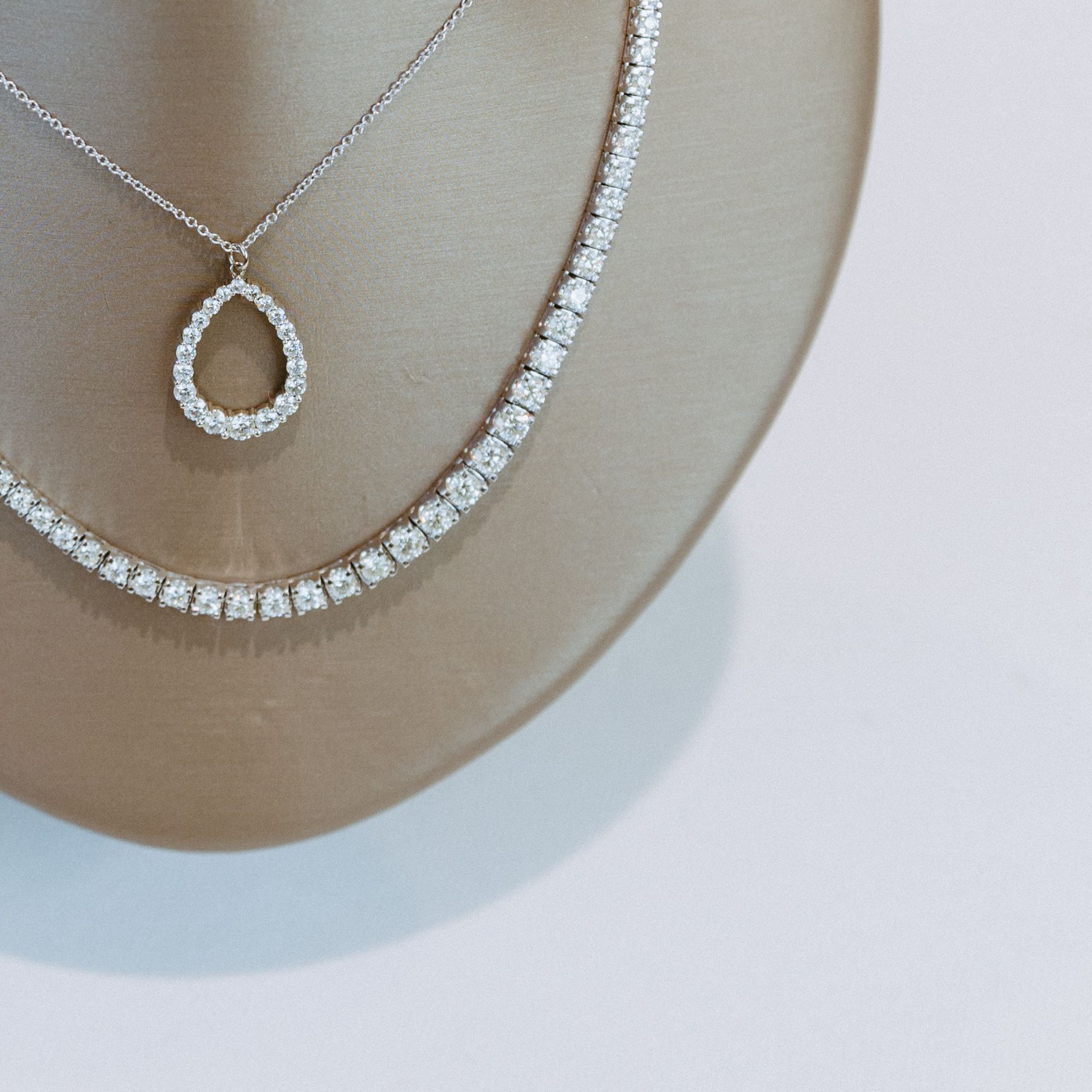 Two diamond necklaces on a mannequin. One has a teardrop pendant.