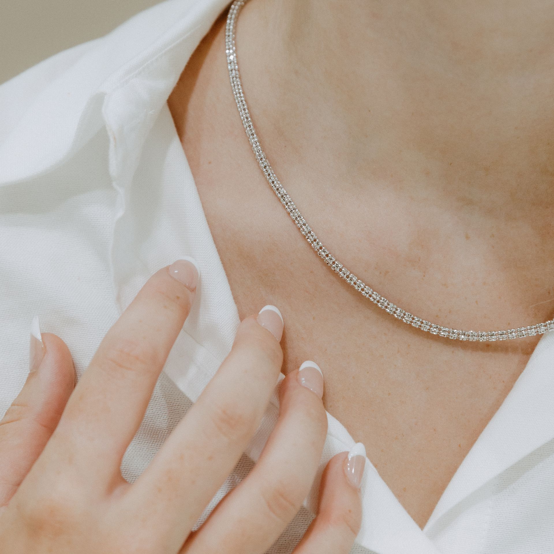 Person wearing a diamond tennis necklace, close-up on neck and hand touching white shirt.