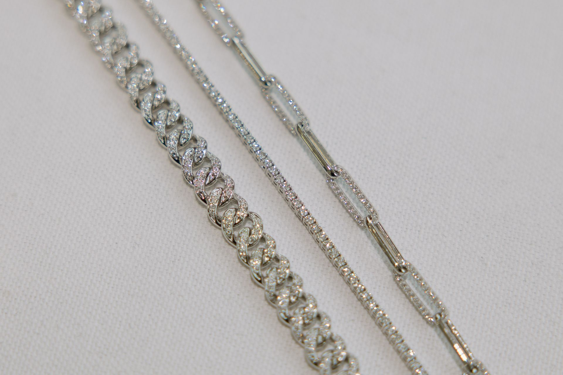 Three silver necklaces on a white surface, featuring different chain styles: a textured braid, a thin strand, and an oval link.