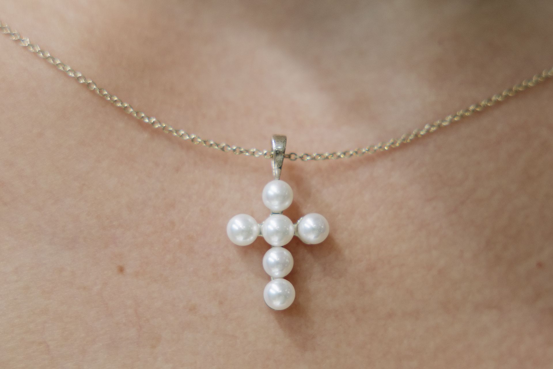 Pearl cross pendant on a gold chain, resting on a person's neck.