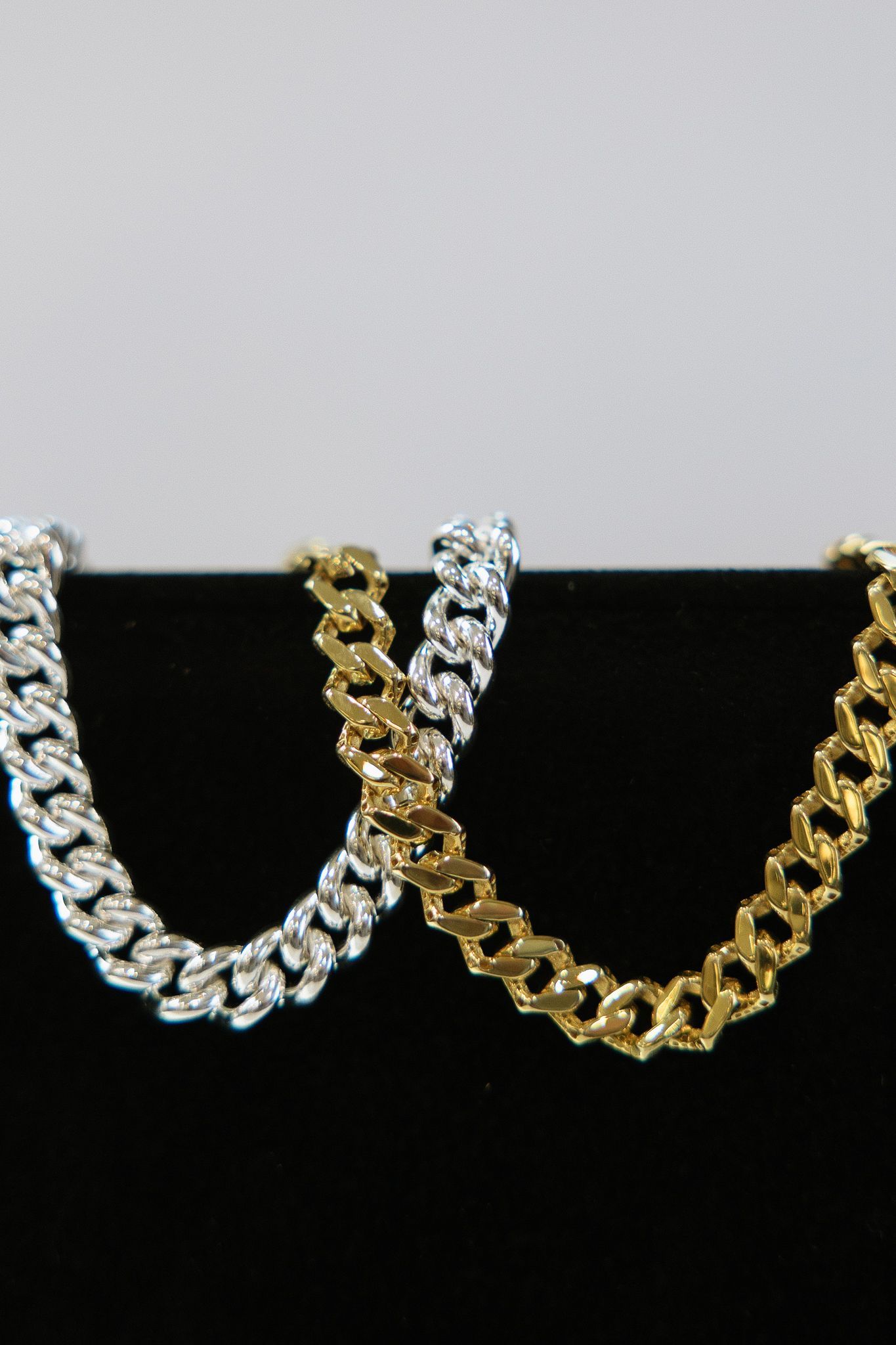 Two gold and silver curb chain necklaces against a black background.
