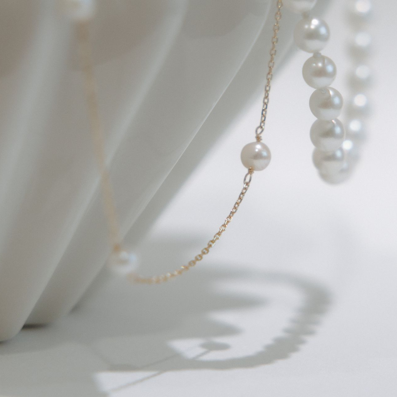 Two delicate necklaces: one gold chain with a single gem, the other silver with a teardrop pendant.