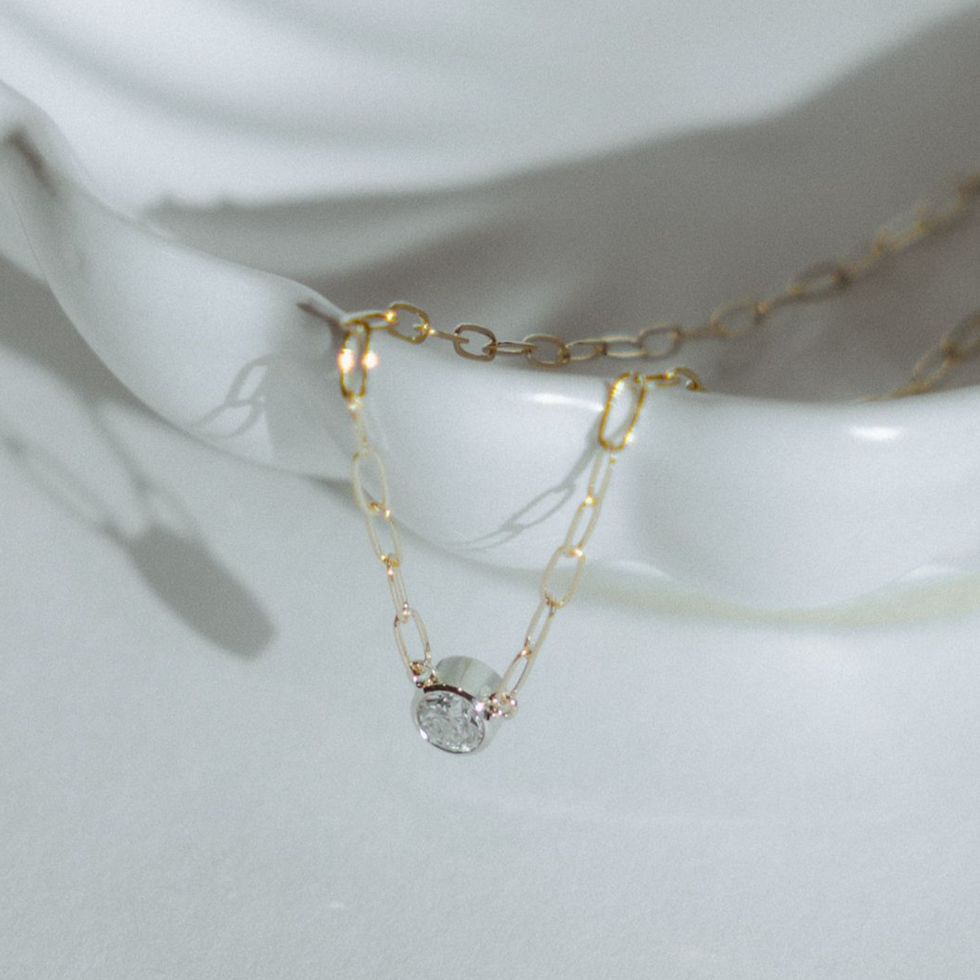 Gold necklace with a small pendant rests in a white, decorative shell.