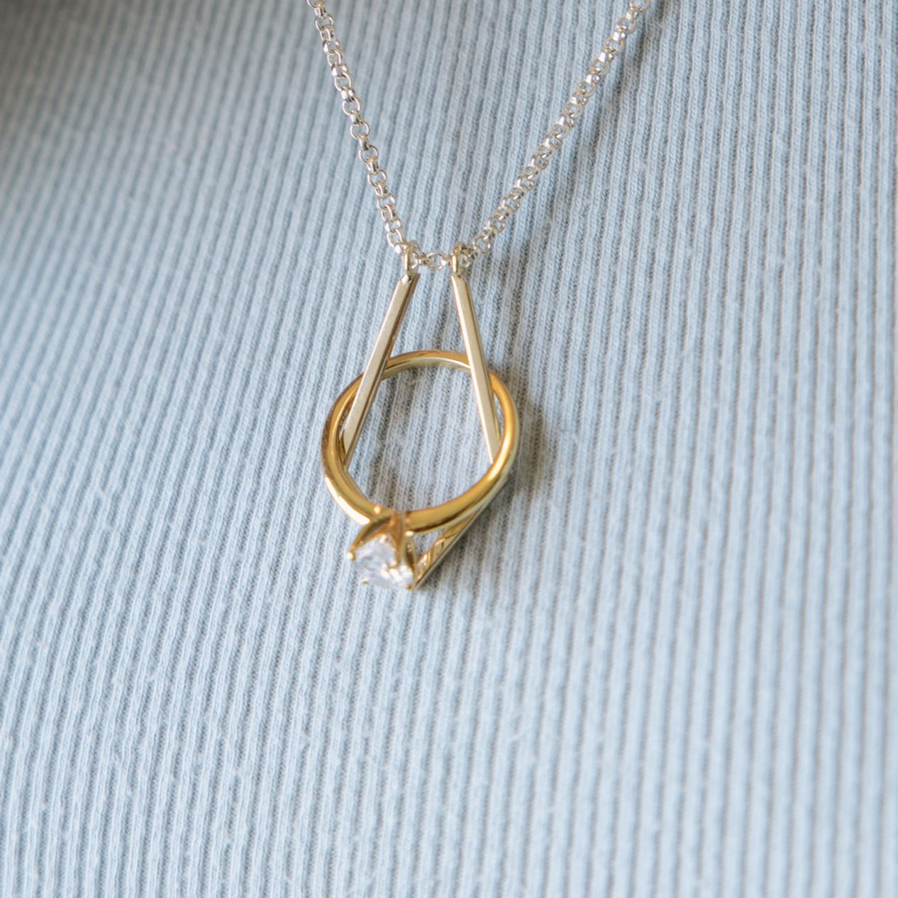 Woman holding a silver necklace with a gold pendant, wearing a light blue shirt.