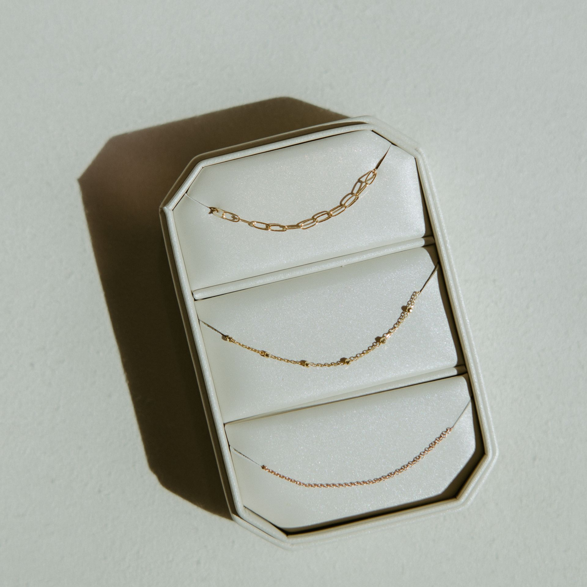 Jewelry box with three gold necklaces on a white surface. Brown box with octagonal shape.