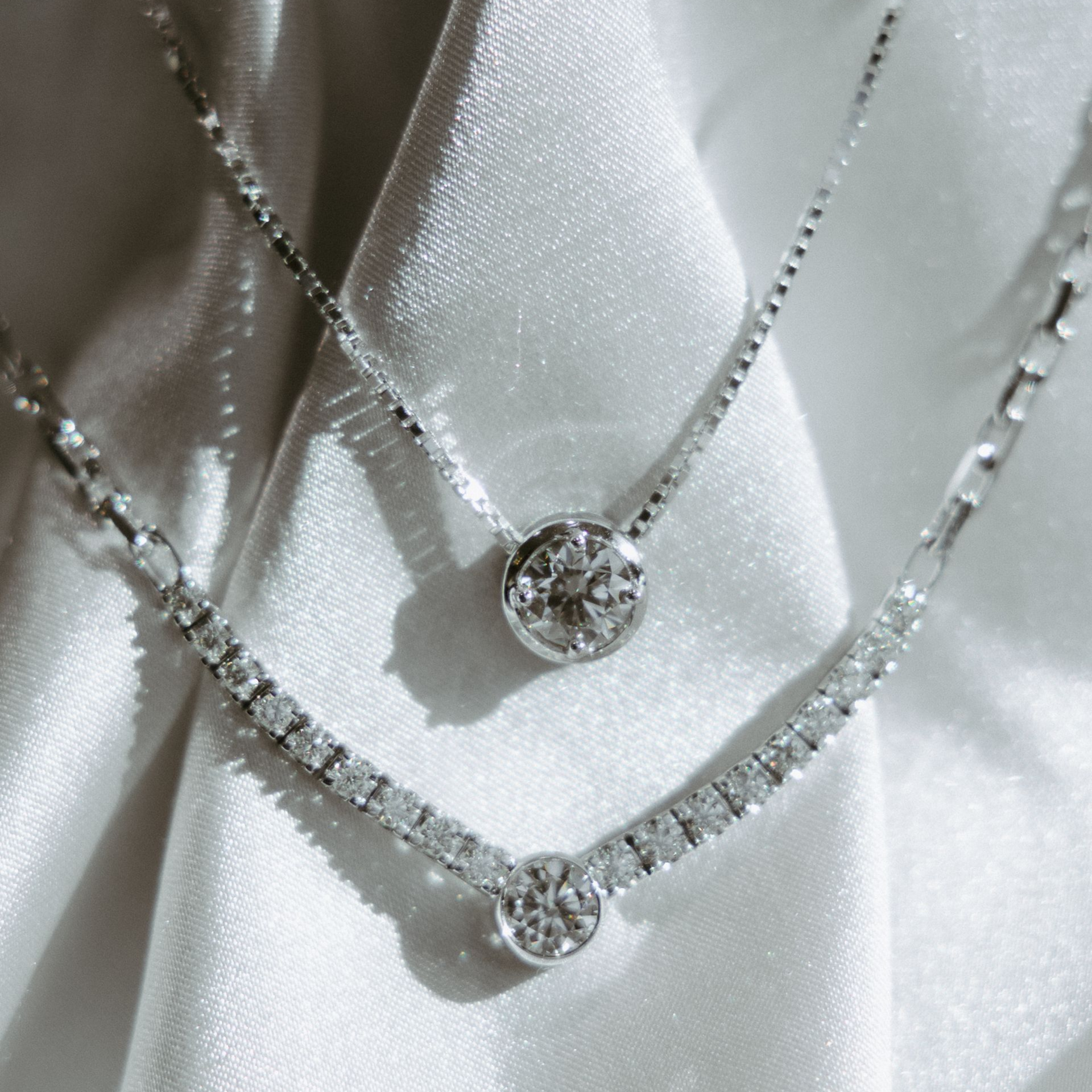 Two diamond necklaces on white satin fabric.