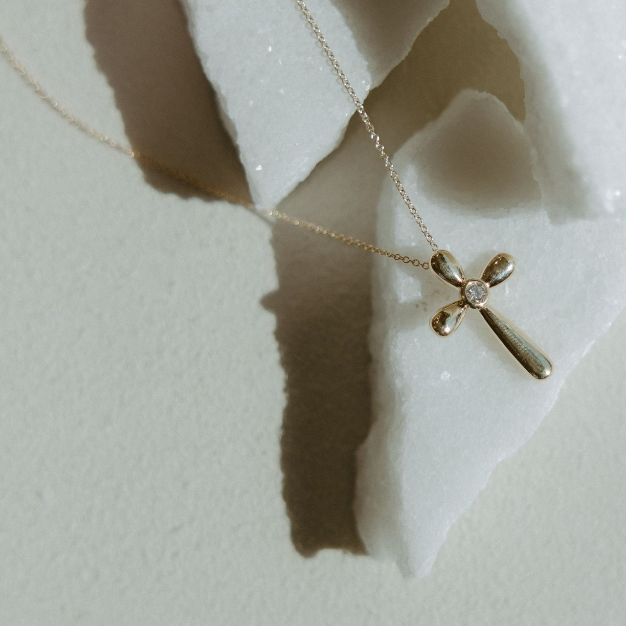 Gold cross pendant necklace on white, textured surface.