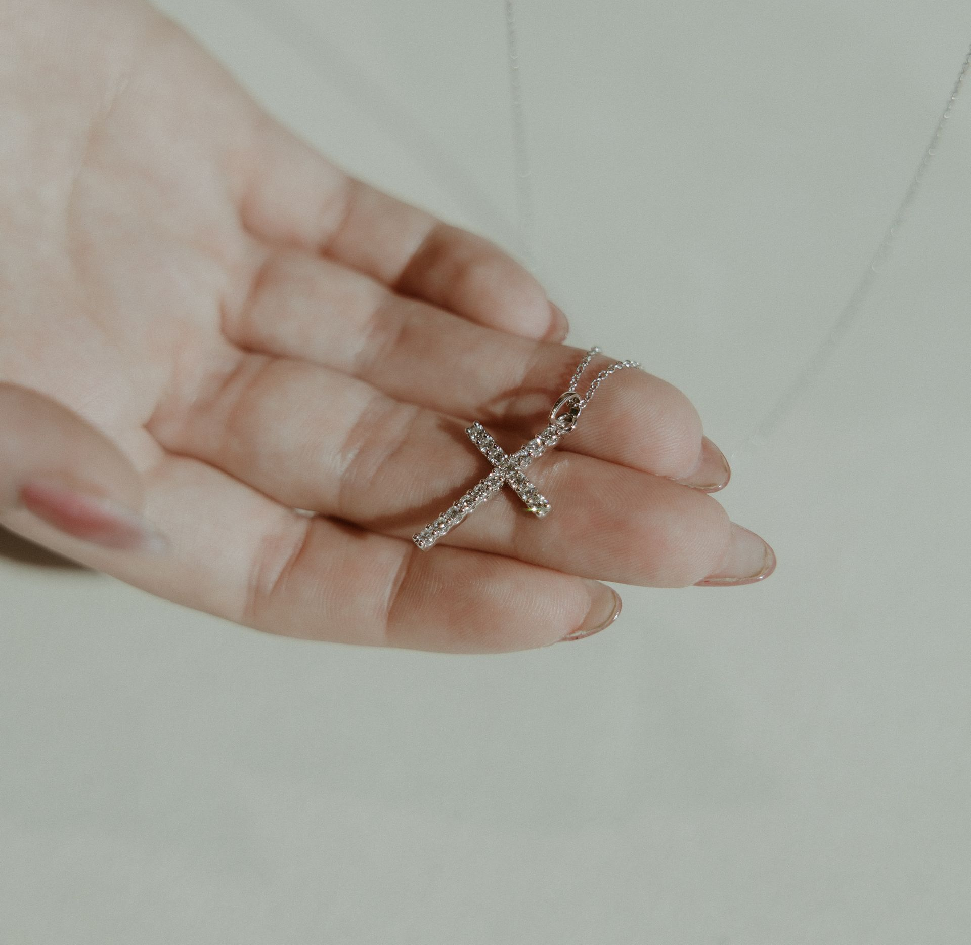 Hands holding a silver cross necklace.