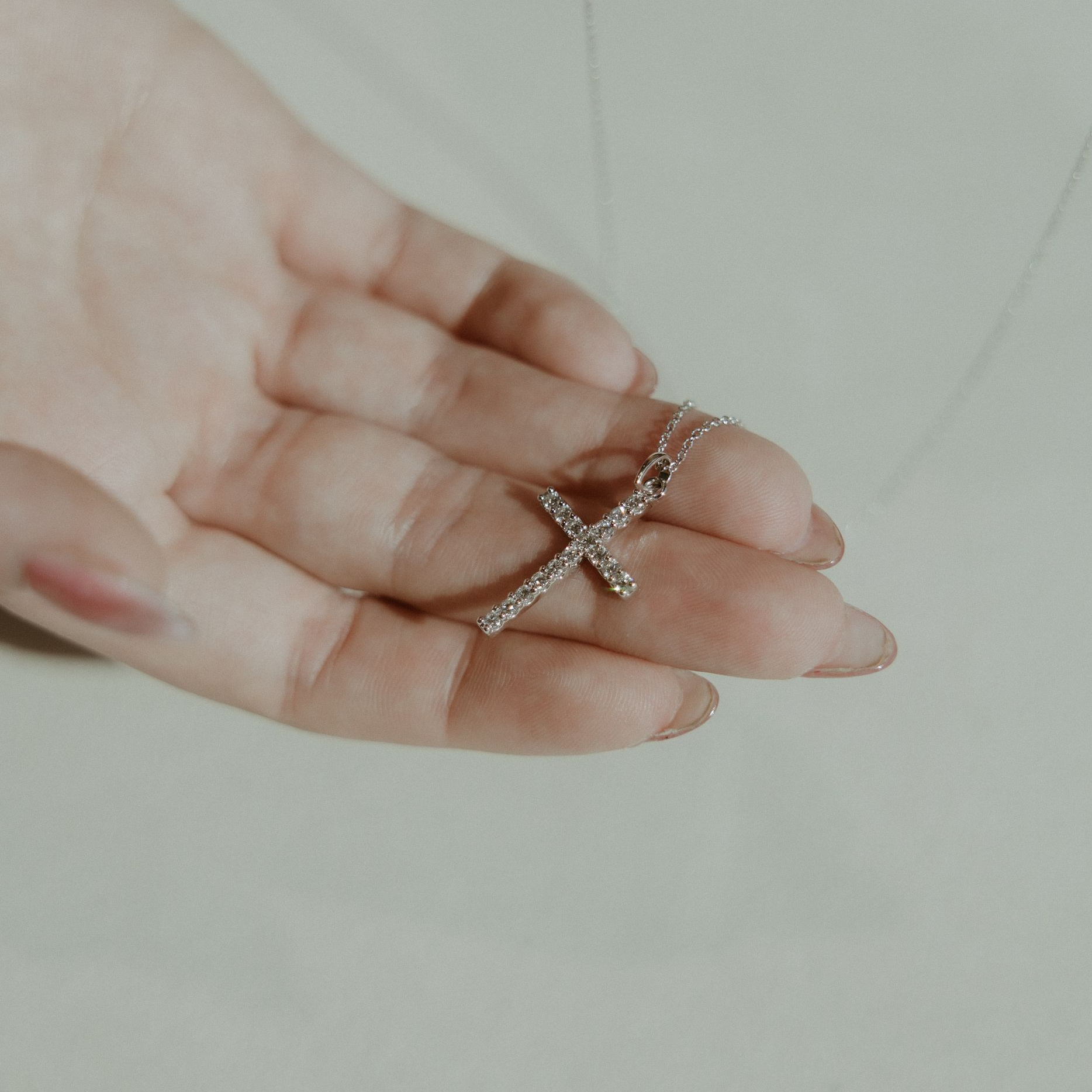 Hands holding a silver cross necklace.