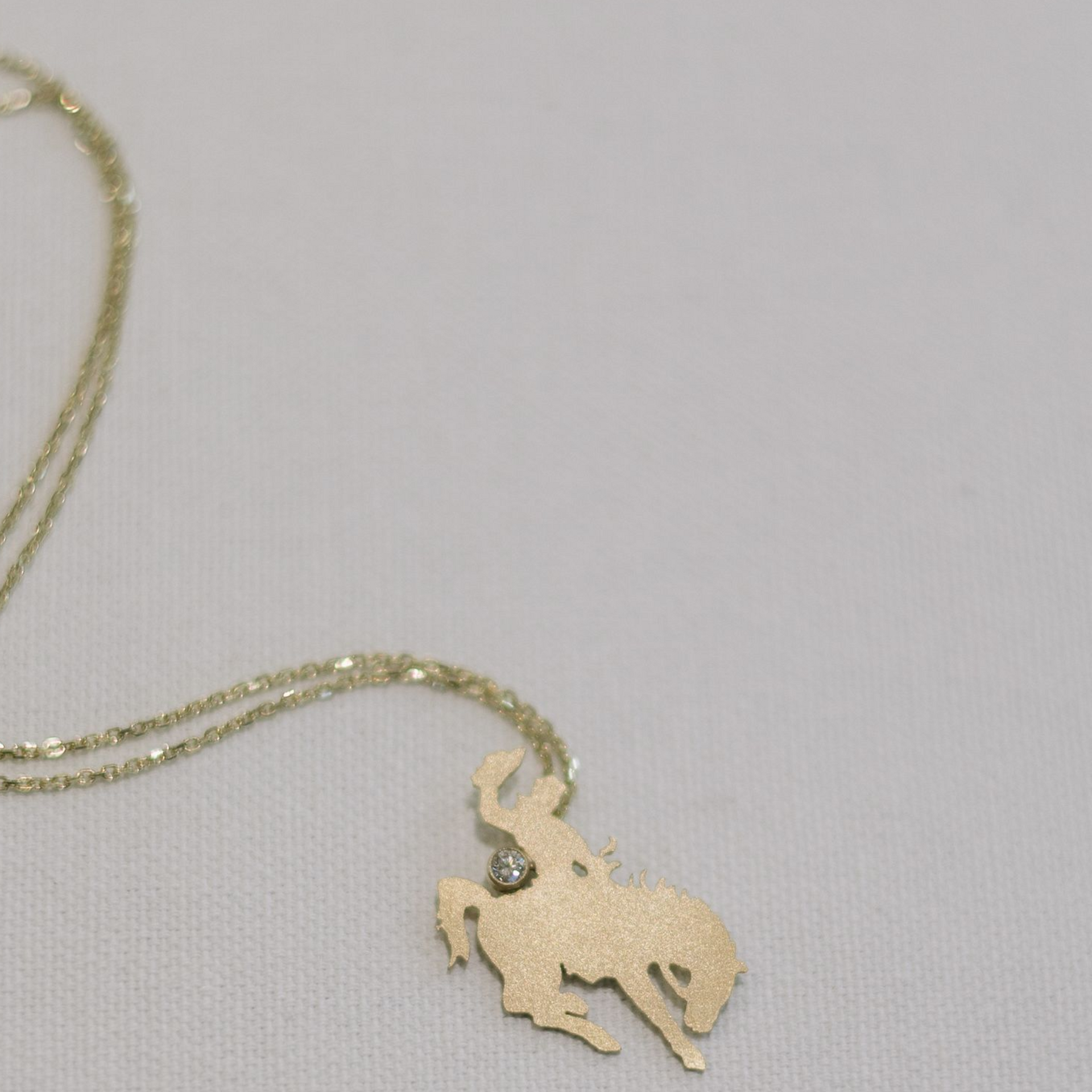 Gold necklace with a cowboy silhouette pendant on a white background.