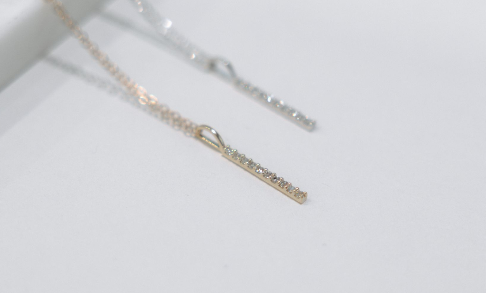 Two delicate necklaces, one gold and one silver, with a vertical bar pendant on a white surface.