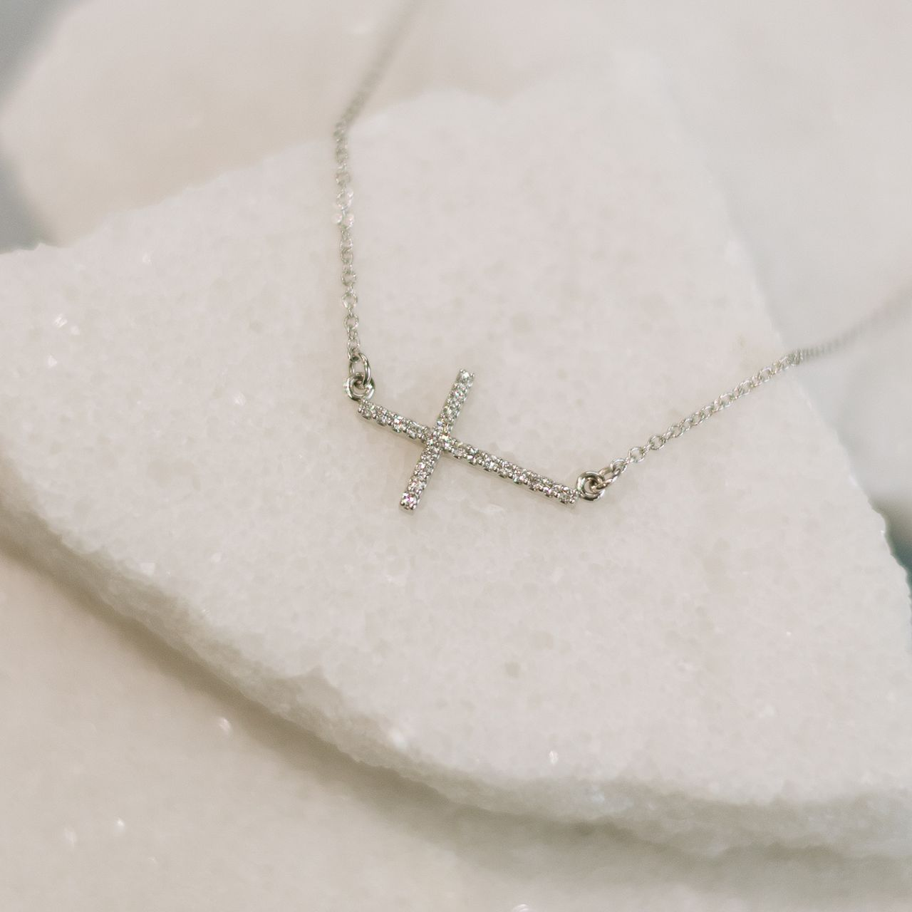 Silver necklace with a cross pendant resting on white, textured stone pieces.