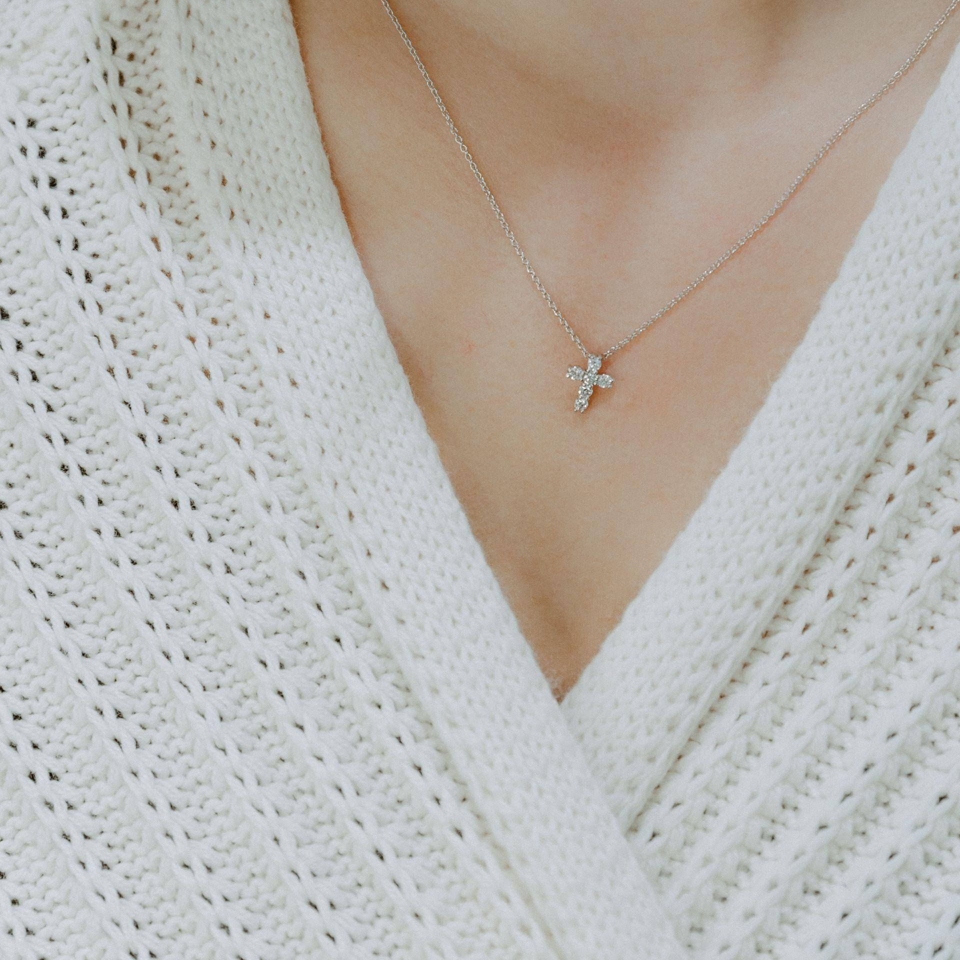 Person wearing a white knitted sweater and a small cross necklace.